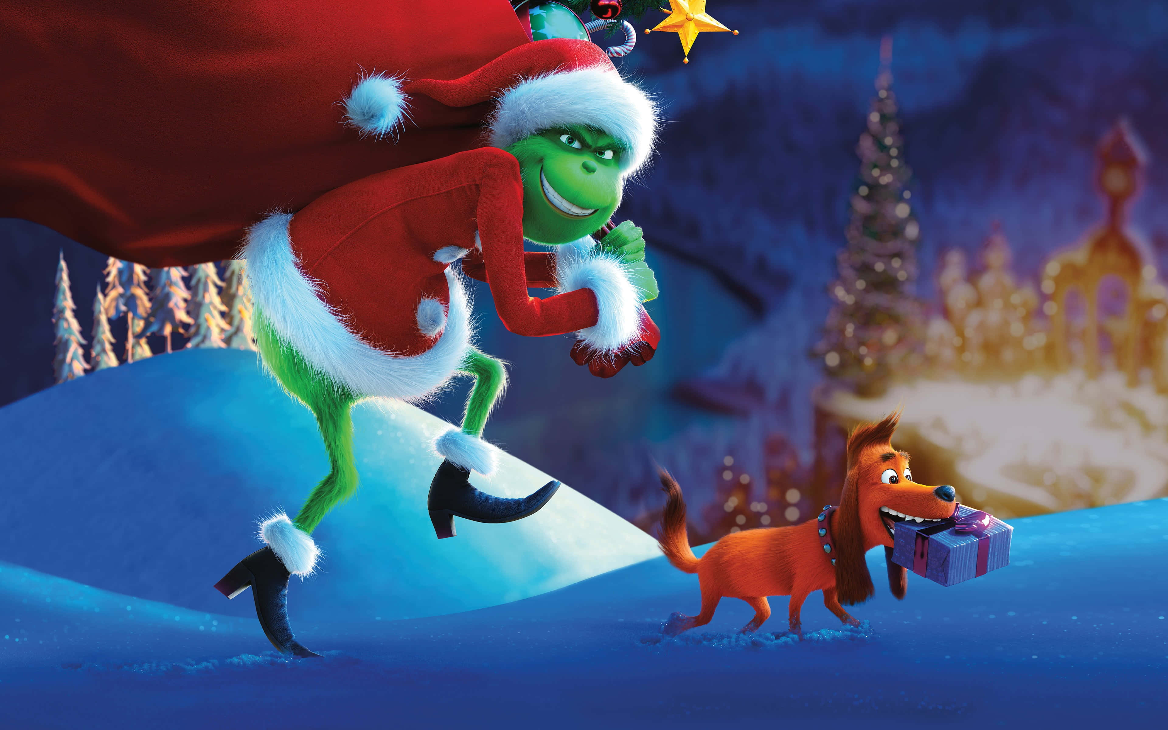 Cute Grinch 桌布 壁紙 — 聖誕老人裝扮的鬼靈精帶著狗在雪地上跳躍，狗叼著禮物，背景是節日氣氛濃厚的冬日小鎮。