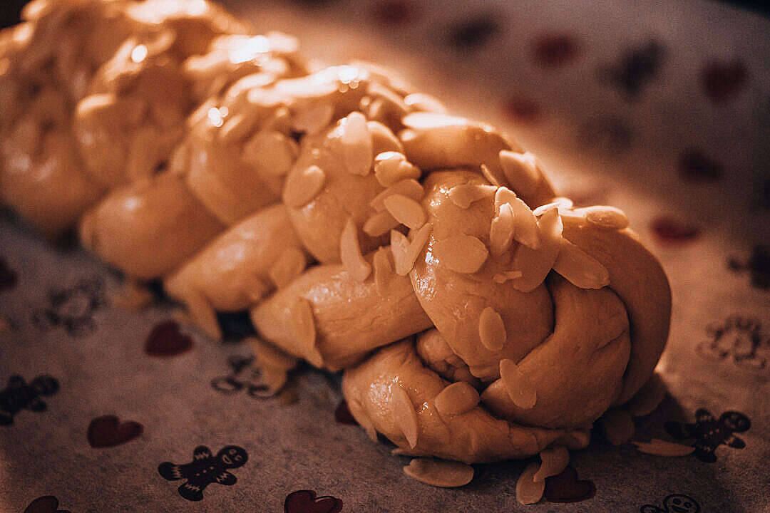 聖誕麵包配精美烘焙紙 壁紙 — 一個金黃色的辮子麵包，上面放有切片杏仁，放在圖案布上，在溫暖的燈光下。