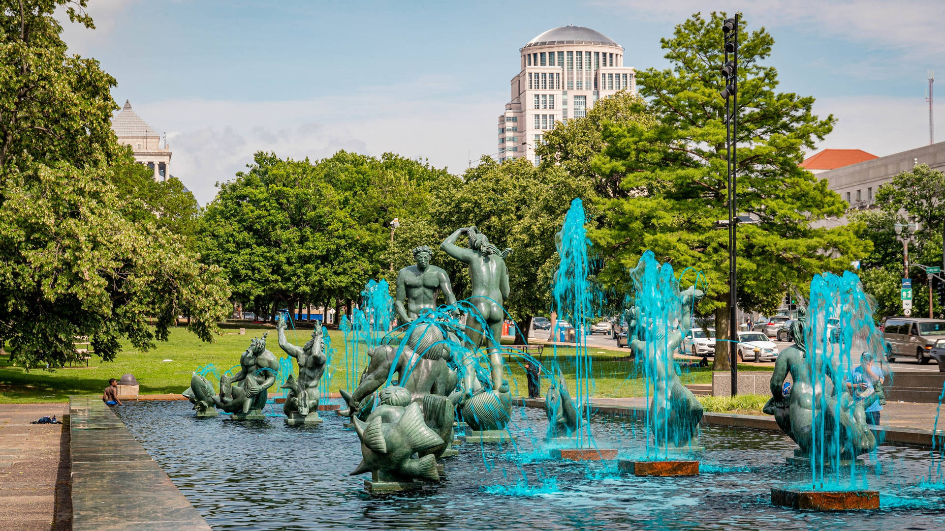城市公園中的青銅噴泉和水柱，綠樹和建築。