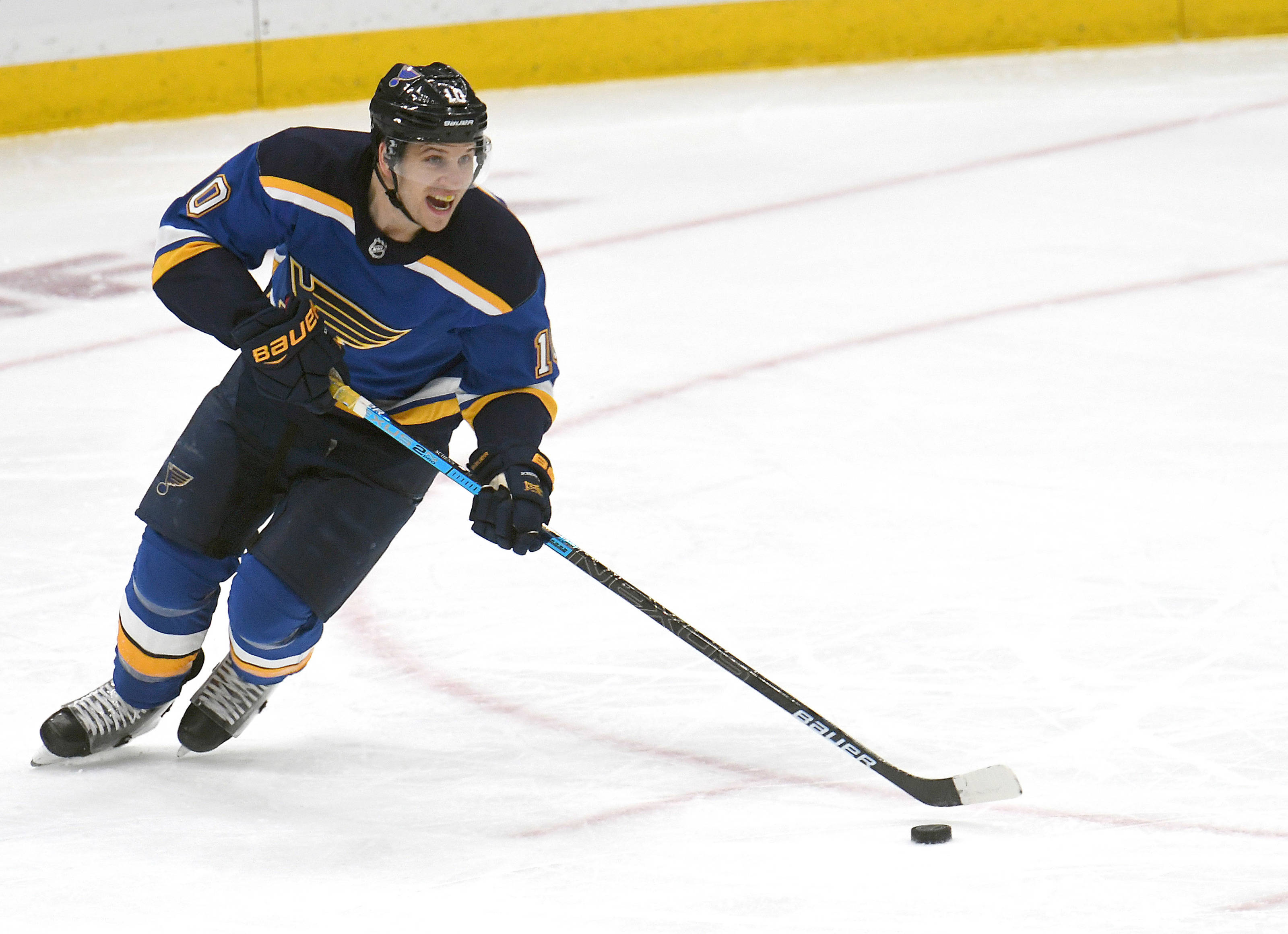聖路易斯藍調隊布雷登·謝恩 NHL 2019 賽事精彩照片 壁紙 — 一名身穿藍色和金色球衣的冰球運動員，在冰場上拿著球棍激烈地向前傾斜滑行。