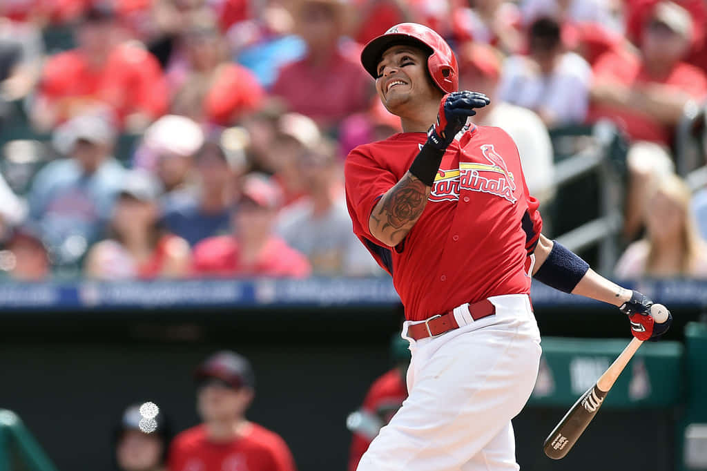 身穿紅色 Cardinals 球衣的棒球手在人群背景下揮棒。