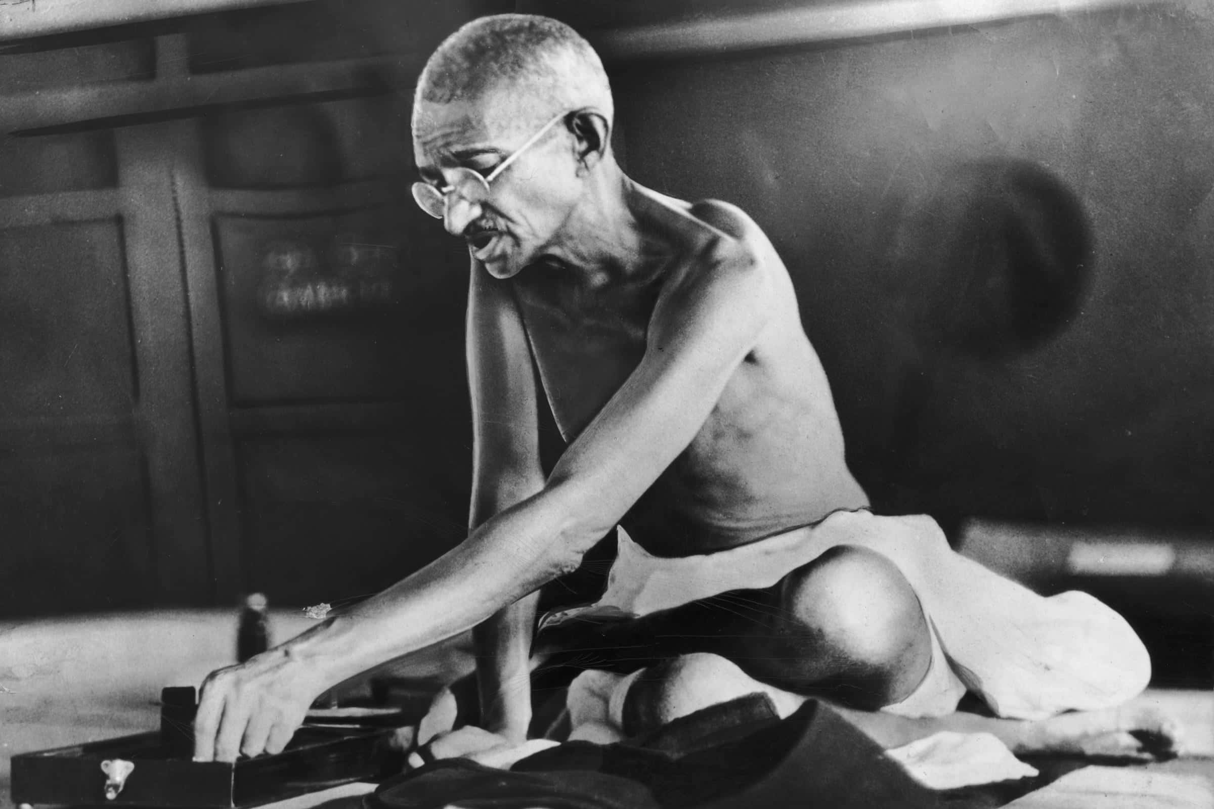 Mahatma Gandhi 桌布 壁紙 — 聖雄甘地赤裸上身坐在昏暗的房間裏，專注地用手織機織布。