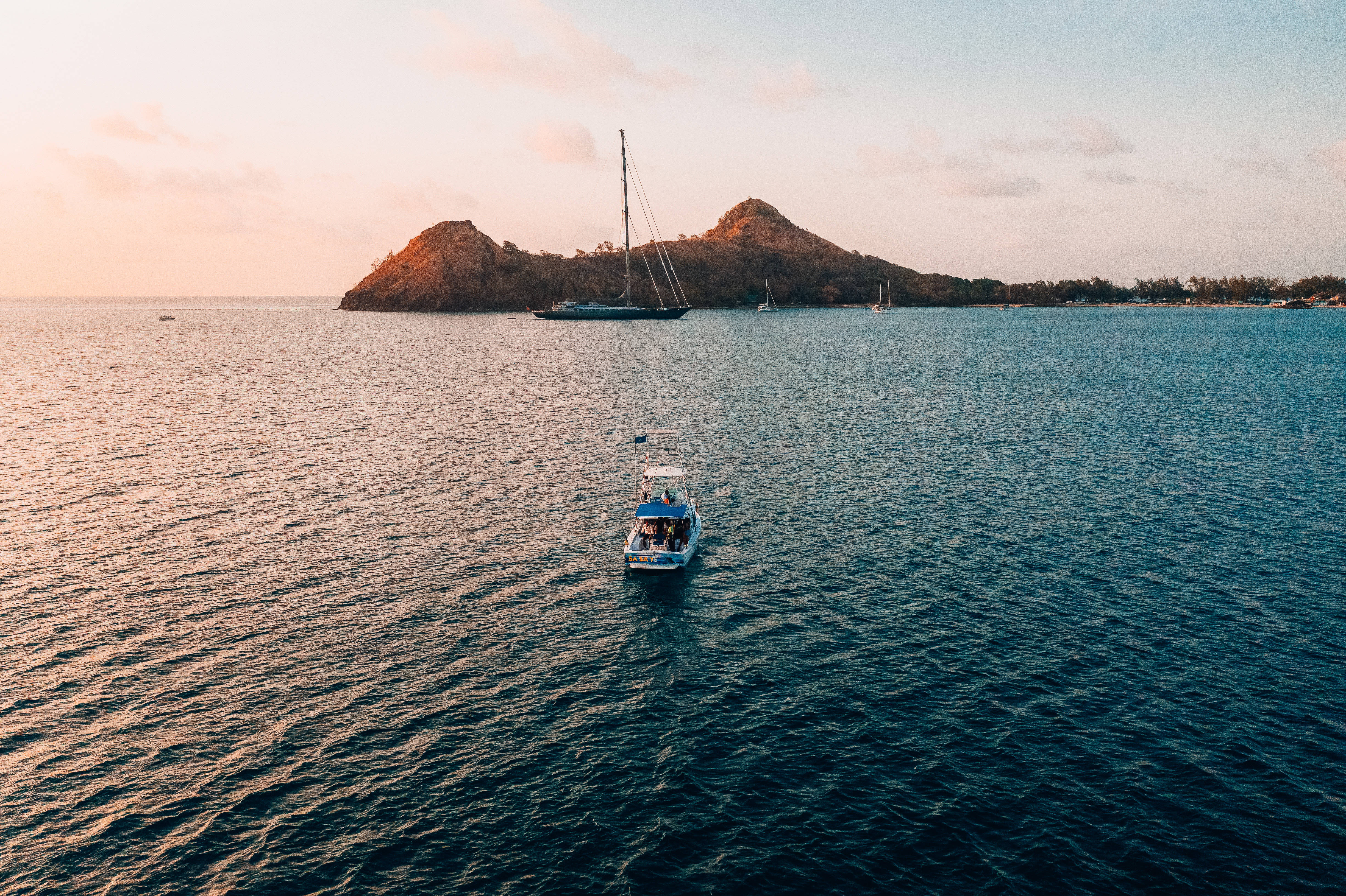 聖露西亞鴿島海岸 壁紙 — 一艘小船在平靜的海面上滑行，駛向沐浴在金色日落光芒中的遙遠火山島。