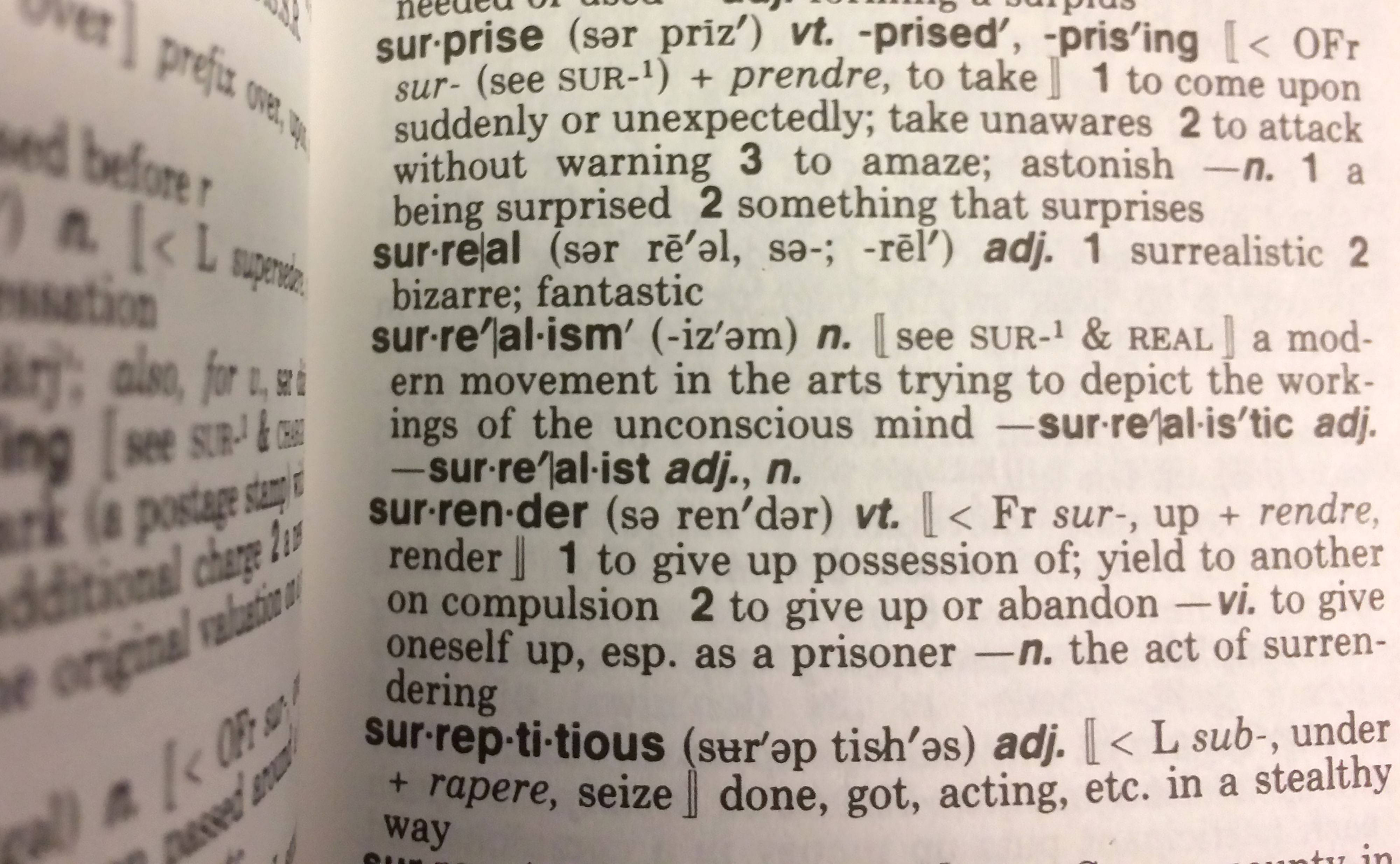 聚焦打開的詞典 壁紙 — 打開字典頁面的特寫，顯示 surprise、surrealism 和 surrender 等詞語的定義，周圍文字模糊。