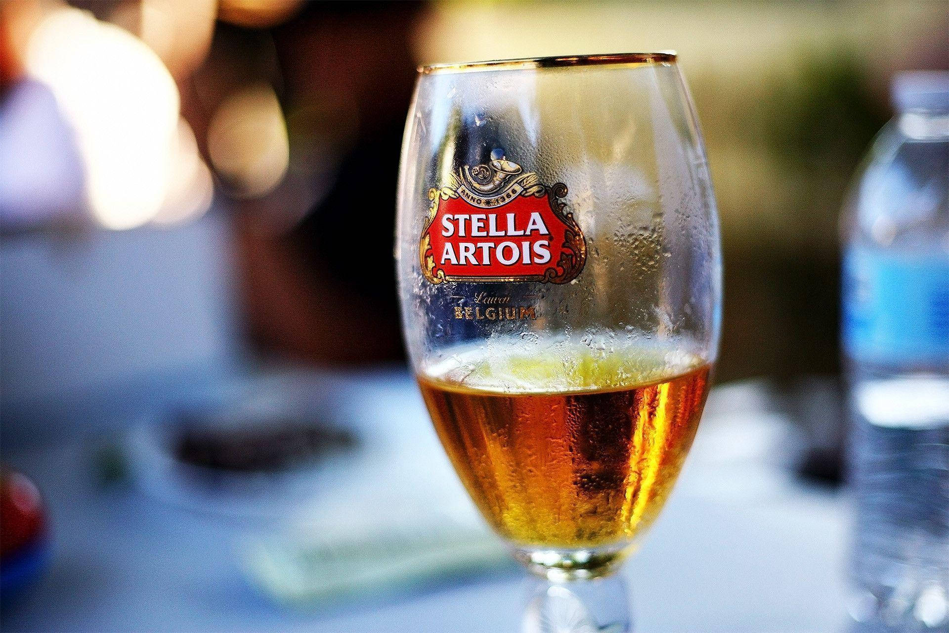 在陽光明媚的戶外桌子上，一杯冰凍的 Stella Artois 啤酒杯，杯身凝結水珠。