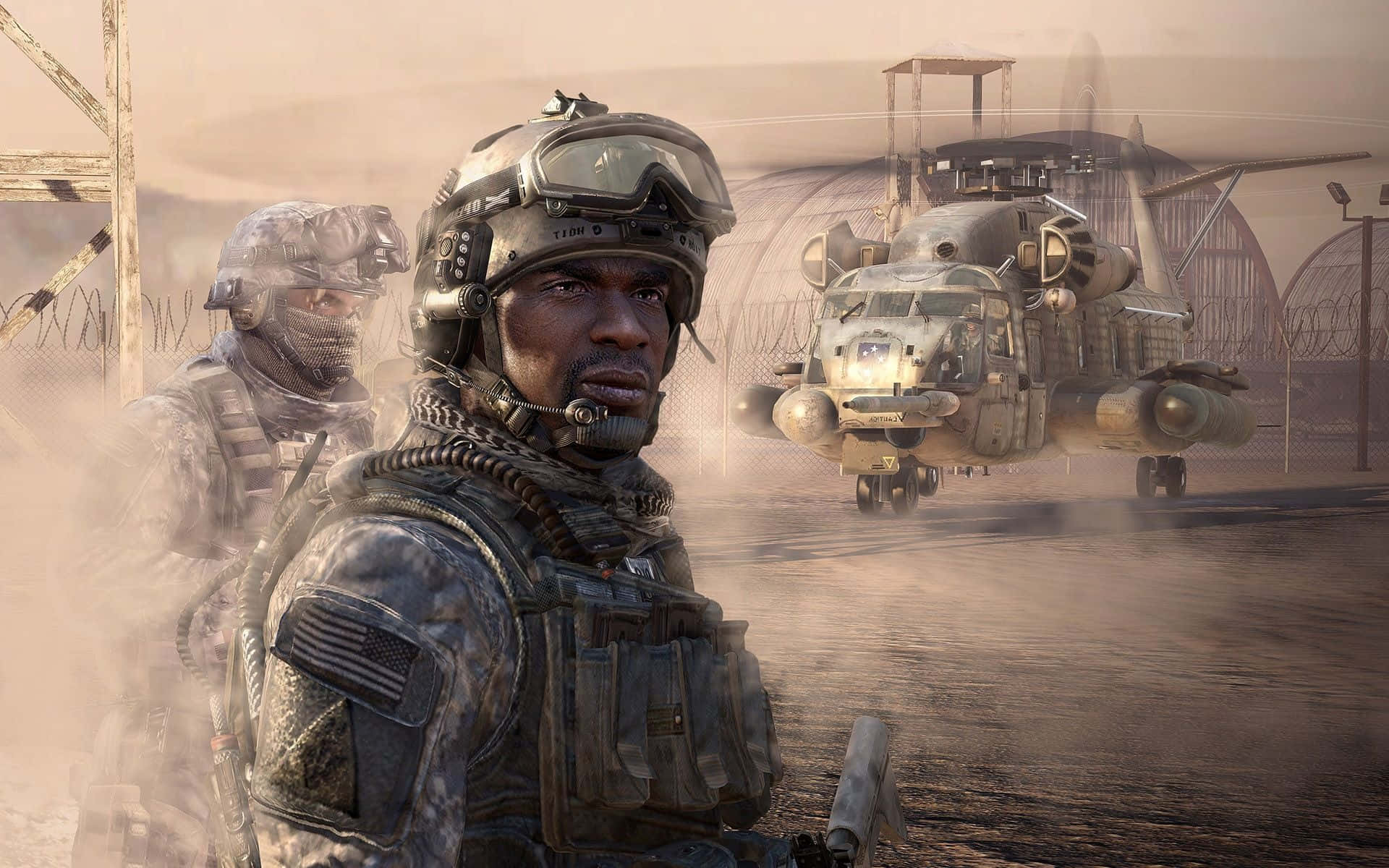 「聯合作戰，共赴使命！Call of Duty！」 壁紙 — 一名身穿沙漠迷彩的士兵警覺地站立，一架軍用直升機在有圍欄的建築群附近的塵霧中降落。