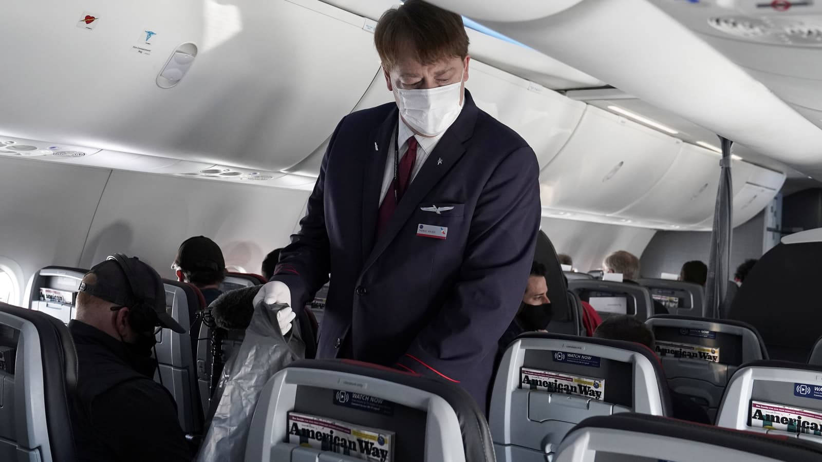 空中服務員戴口罩在美國航空公司飛機上為乘客服務。