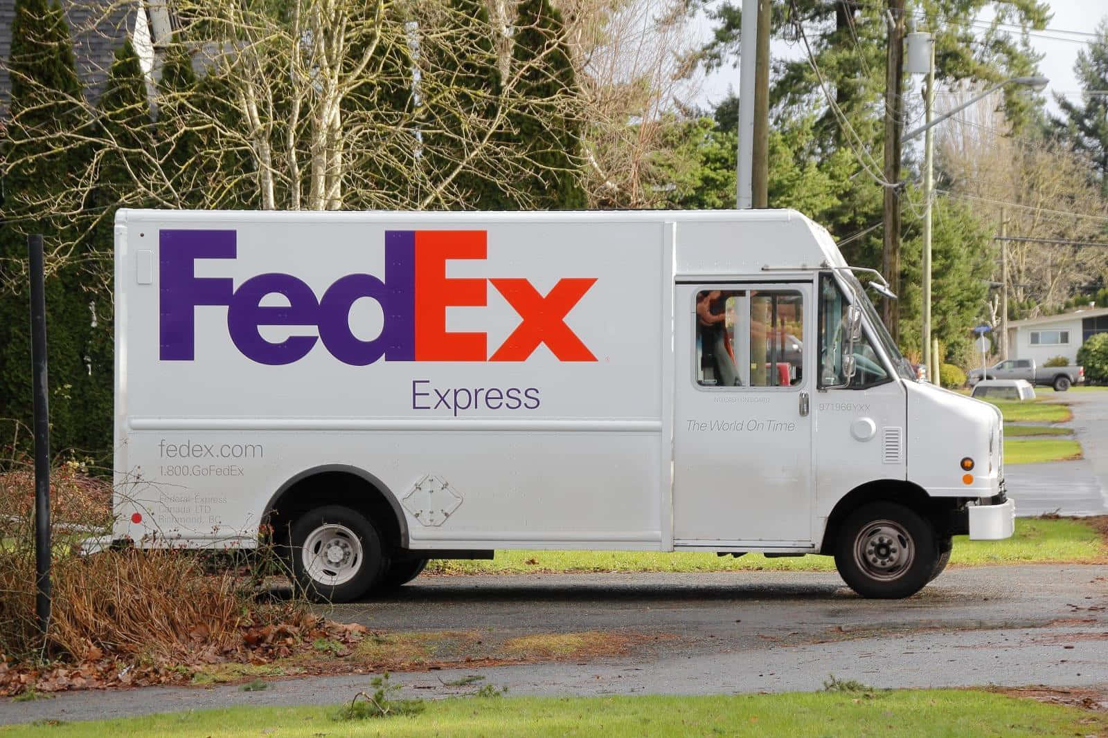 白色FedEx送貨車停在潮濕的郊區街道上，有光禿禿的樹木。