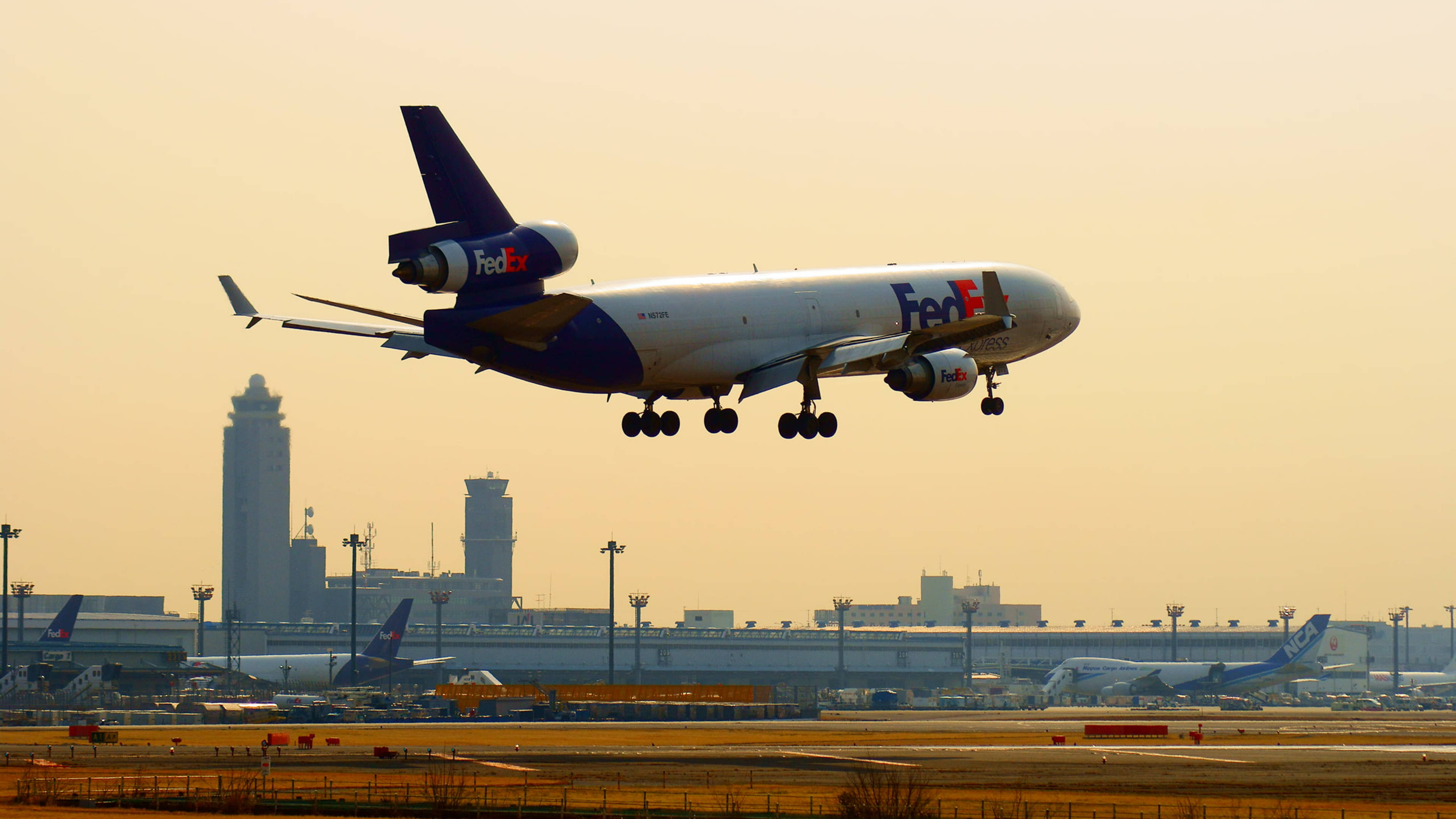 聯邦快遞MD-11起飛 壁紙 — 一架聯邦快遞貨機在機場客運大樓上空，以朦朧的金色日落為背景，下降準備著陸。