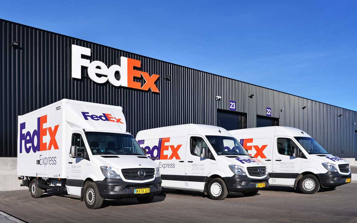 三輛FedEx送貨車停在帶有FedEx標誌的倉庫外。