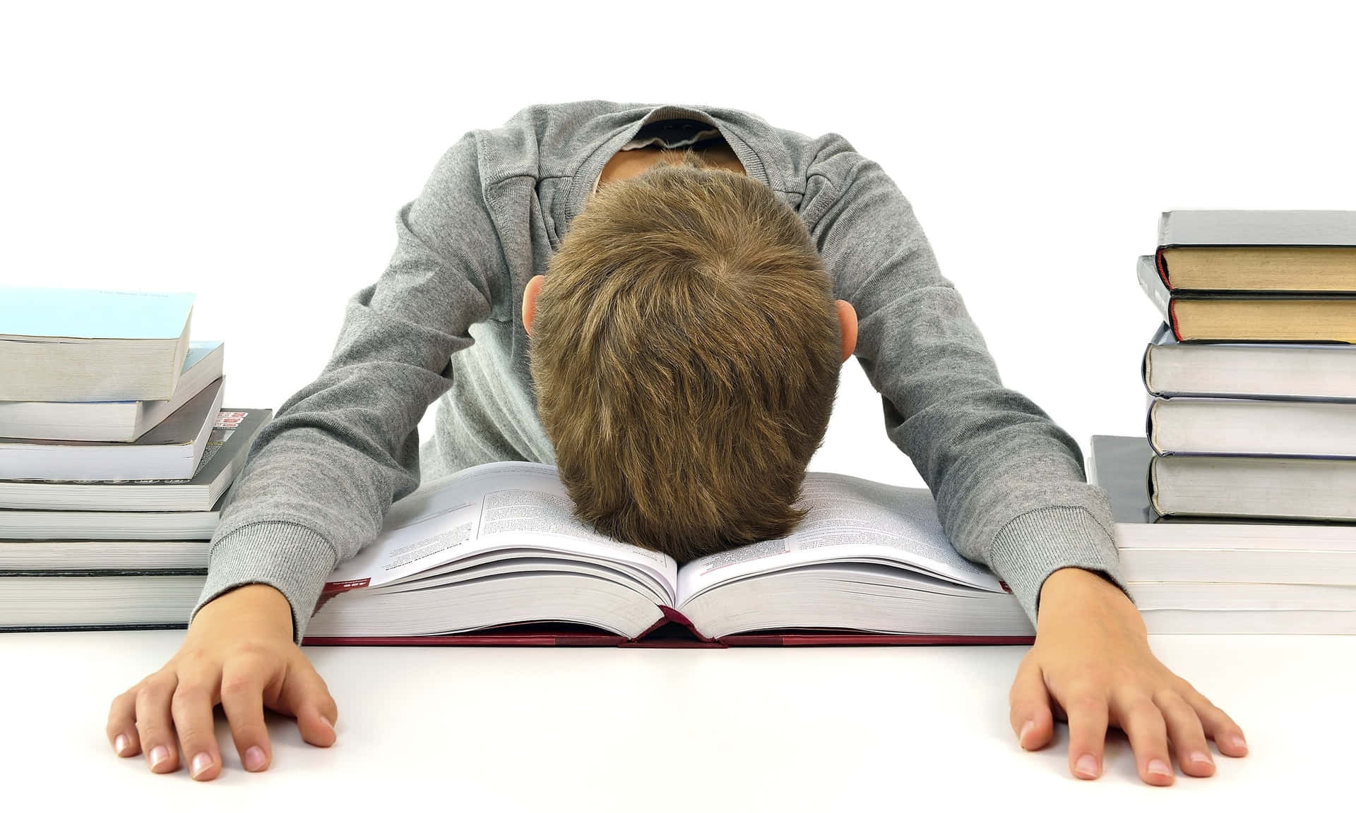 疲倦的學生將頭靠在打開的教科書上，被書堆包圍。