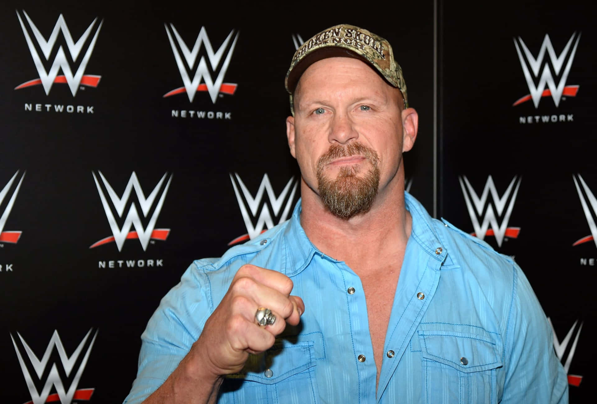 WWE摔角手身穿藍色恤衫戴帽，手指戴戒指擺姿勢。