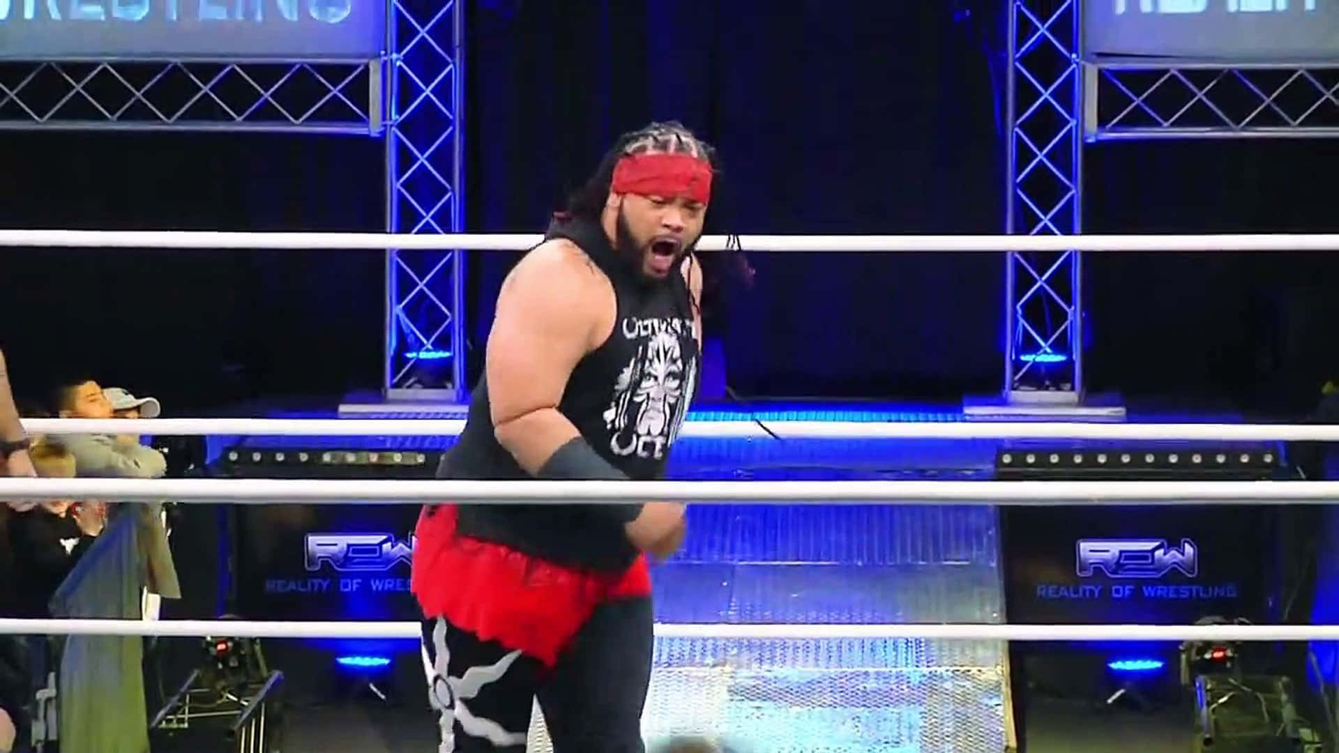 職業摔角手雅各布·法圖 Major League Wrestling 壁紙 — 一位肌肉發達的摔角手，戴著紅色頭帶和黑色背心，在藍色舞台燈光照耀的擂台上咆哮。