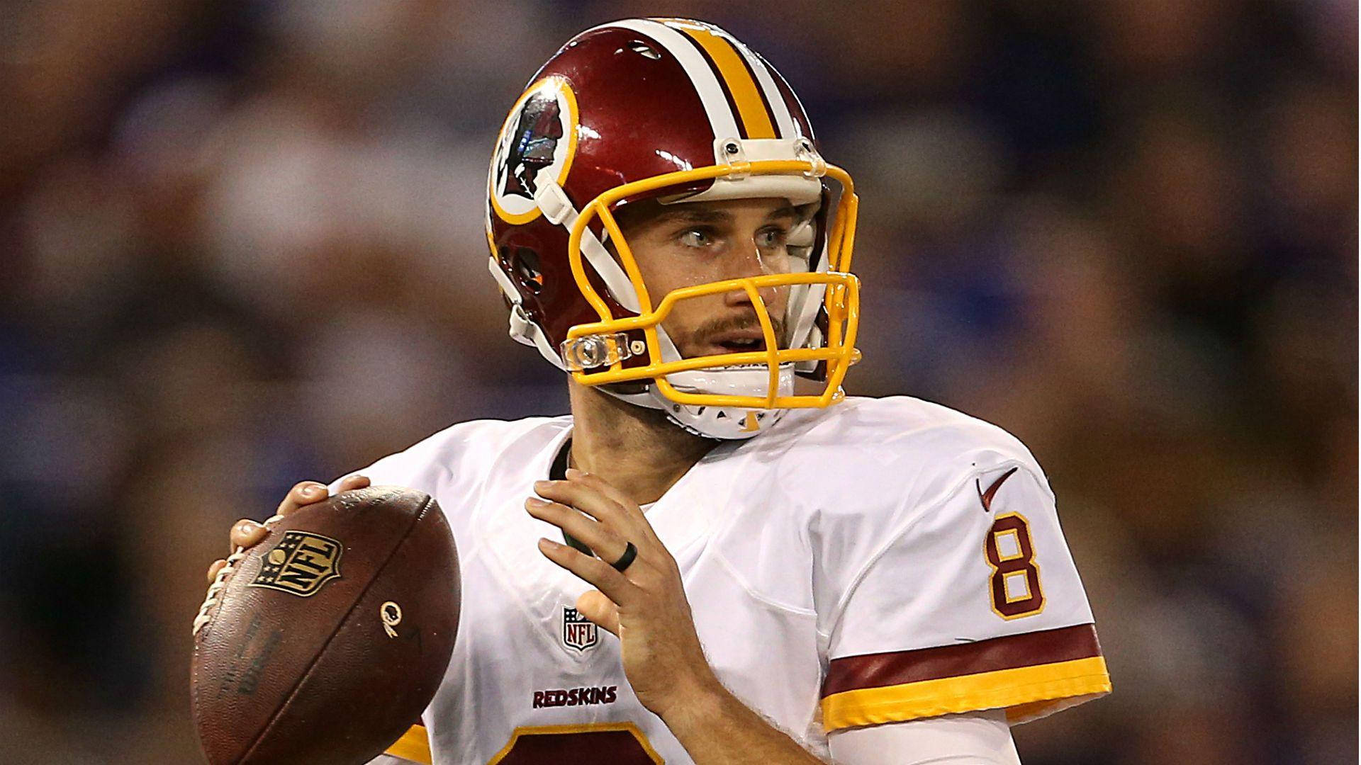 職業美式足球員 Kirk Cousins 壁紙 — 一位專注的華盛頓紅皮四分衛身穿白色8號球衣，在體育場燈光下持球。