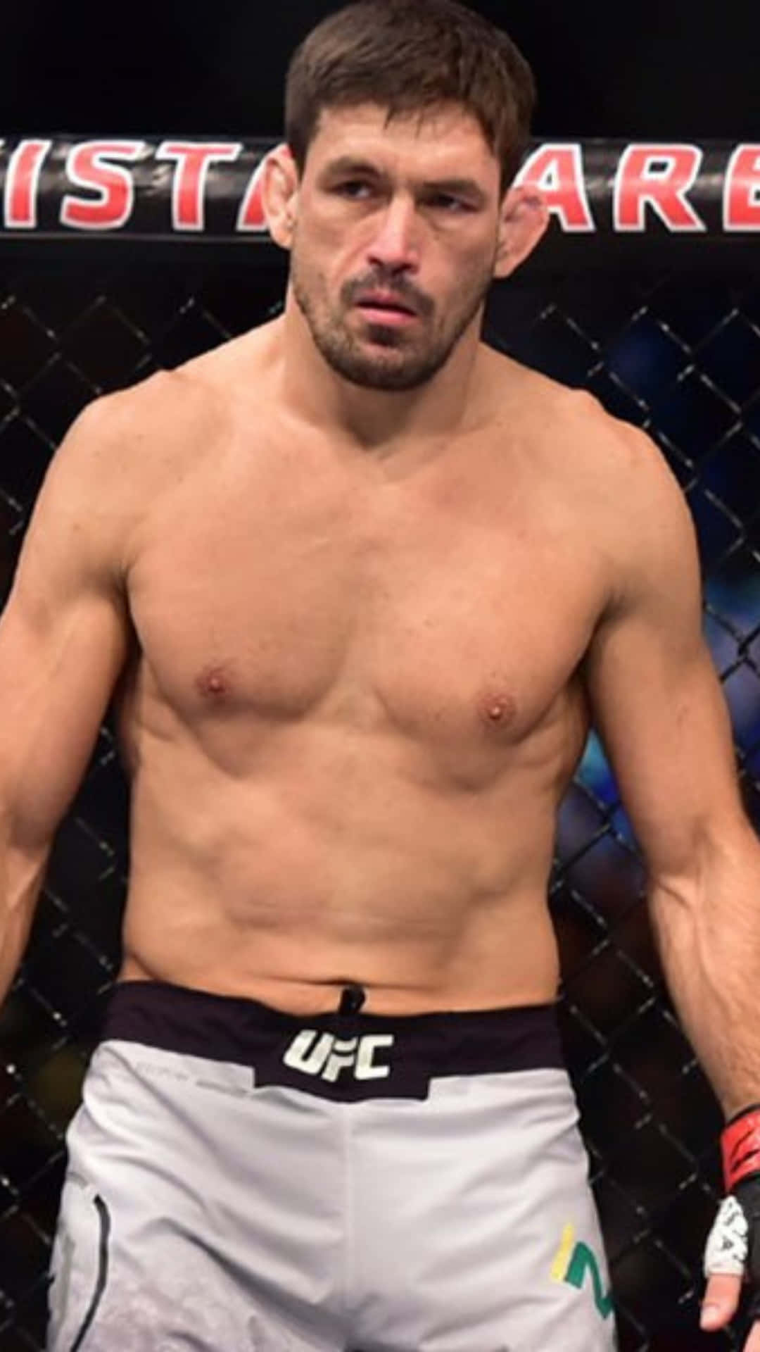 一位赤裸上身的男性MMA拳手穿著白色UFC短褲，在八角籠內。