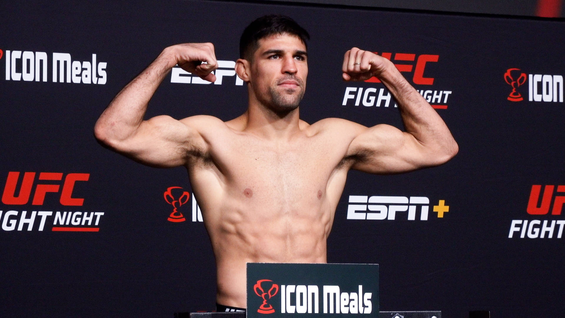 UFC拳手在稱重活動中彎曲手臂，背景有ESPN和ICON Meals標誌。