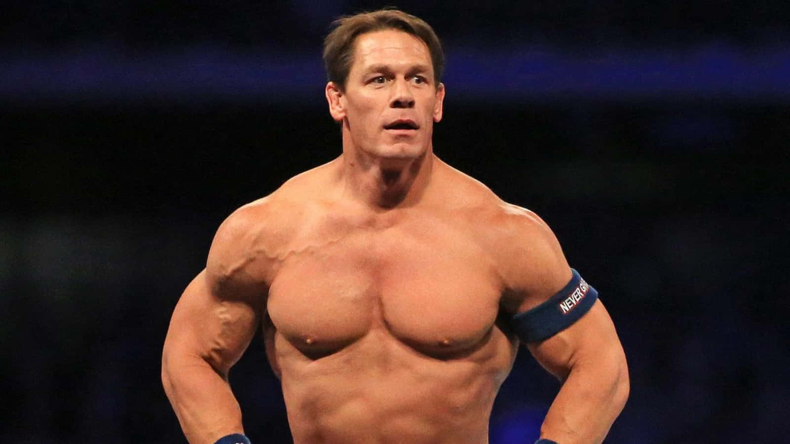 John Cena 桌布 壁紙 — 肌肉發達的摔角手約翰·辛納赤裸上身站在昏暗的場館中，專注力極強，體格分明。