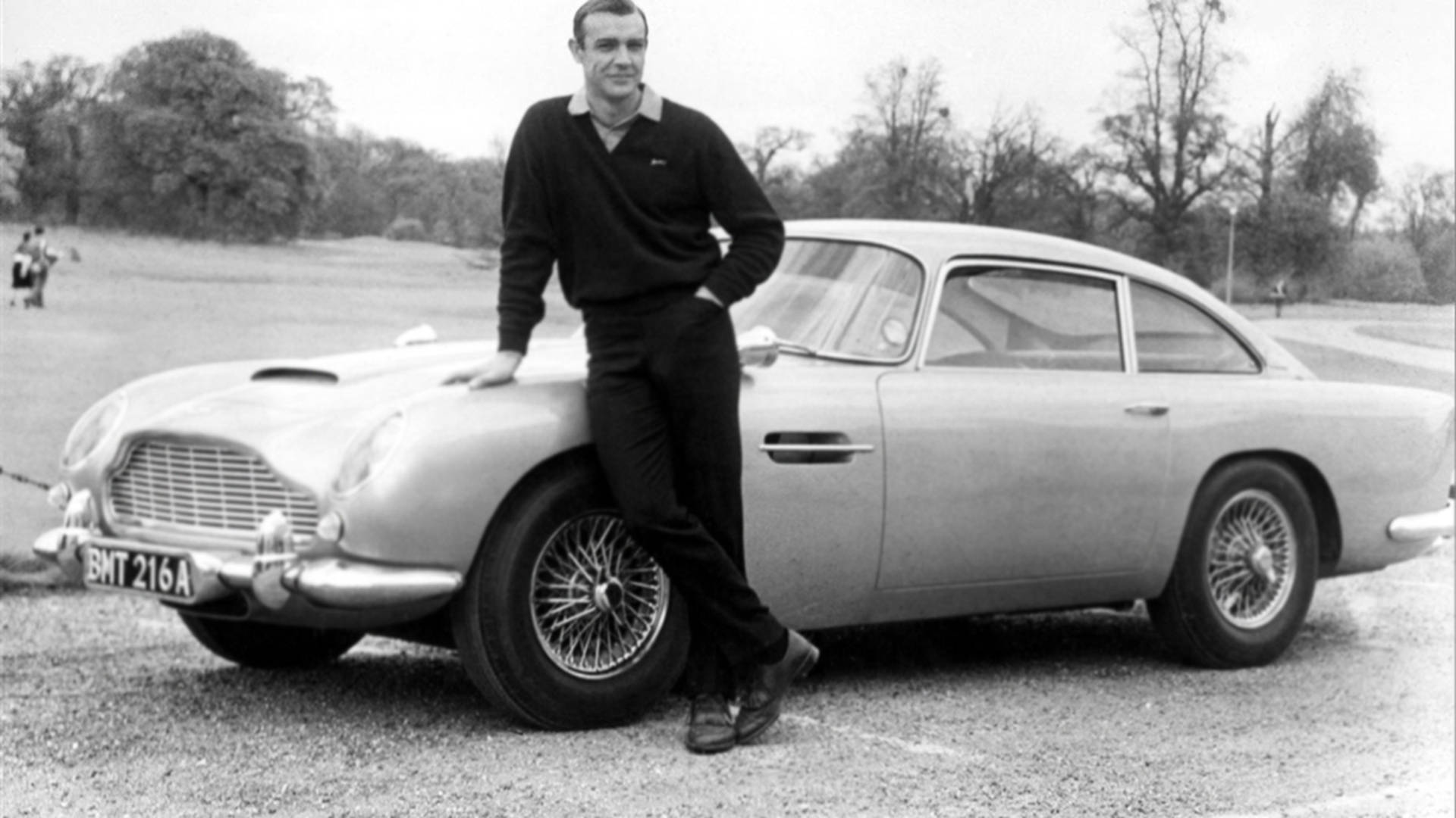 辛·康納利在碎石路上與銀色Aston Martin DB5合影。
