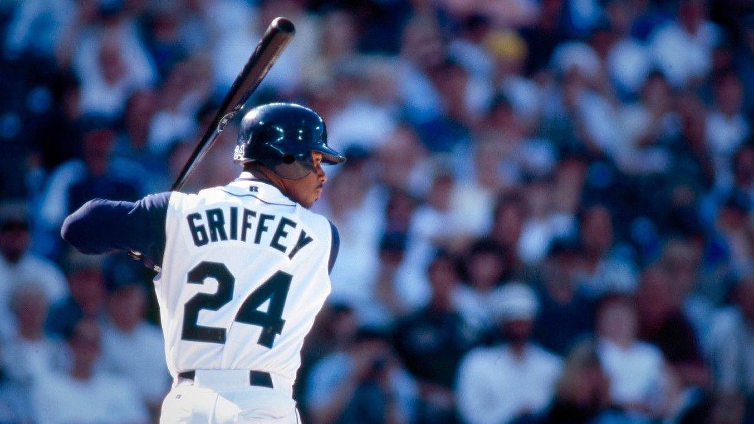 肯·格里菲·小將 擊球準備 壁紙 — 身穿白色球衣的棒球選手Griffey 24號在球場準備揮棒，背景是模糊的人群。