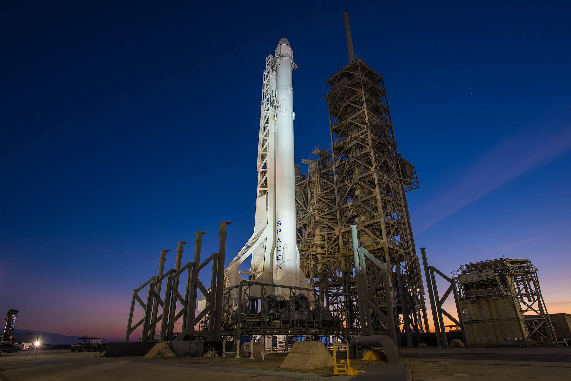 肯尼迪航天中心 SpaceX 猎鹰 9 與龍艙垂直起飛 壁紙 — 一枚SpaceX火箭在發射台上被照亮，背景是帶有深藍色和橙色色調的暮色天空。