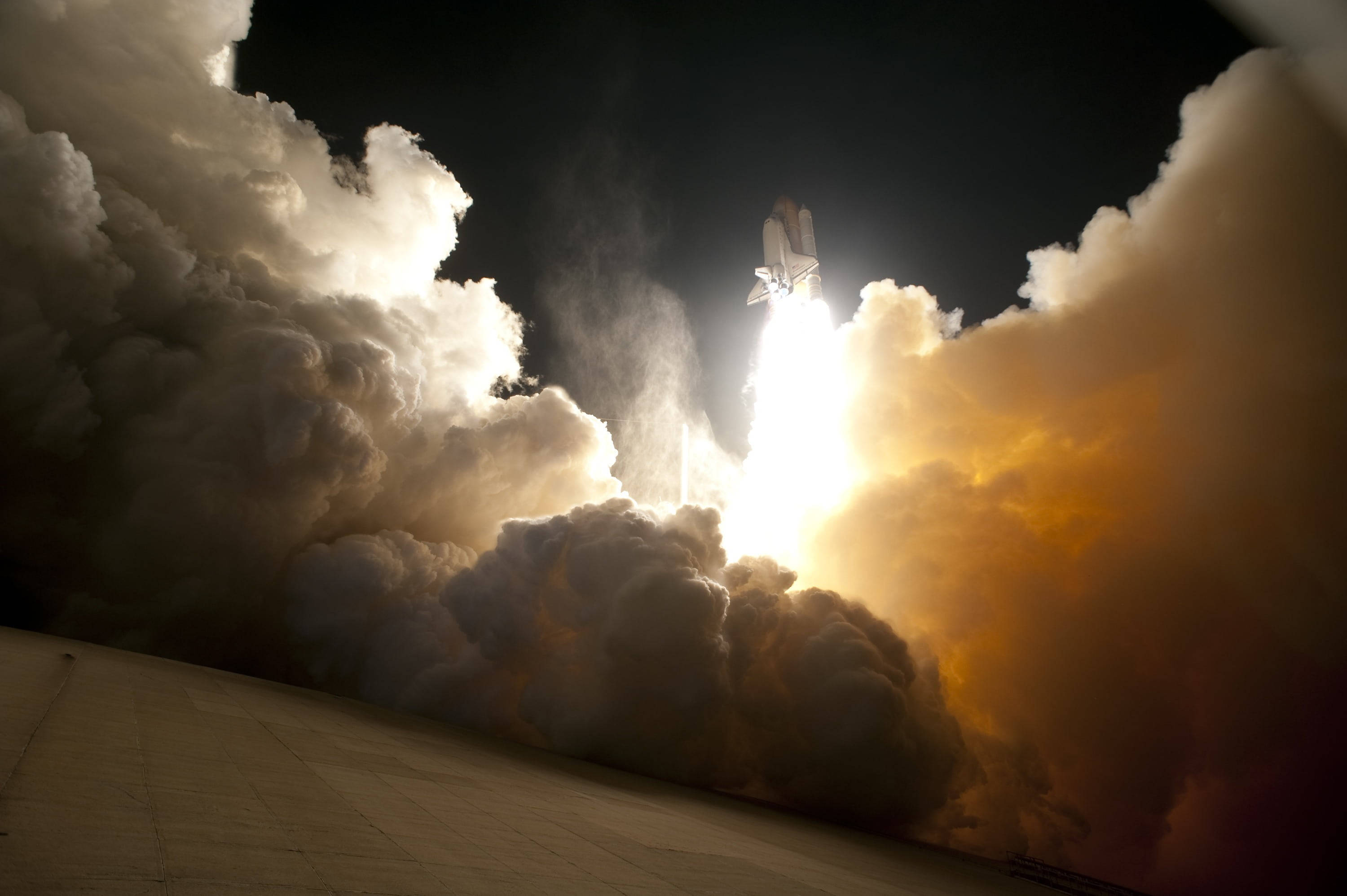 肯尼迪航天中心 夜間濃煙 壁紙 — 一架太空穿梭機在夜間強力穿過雲層上升，身後留下一道明亮的火焰軌跡。