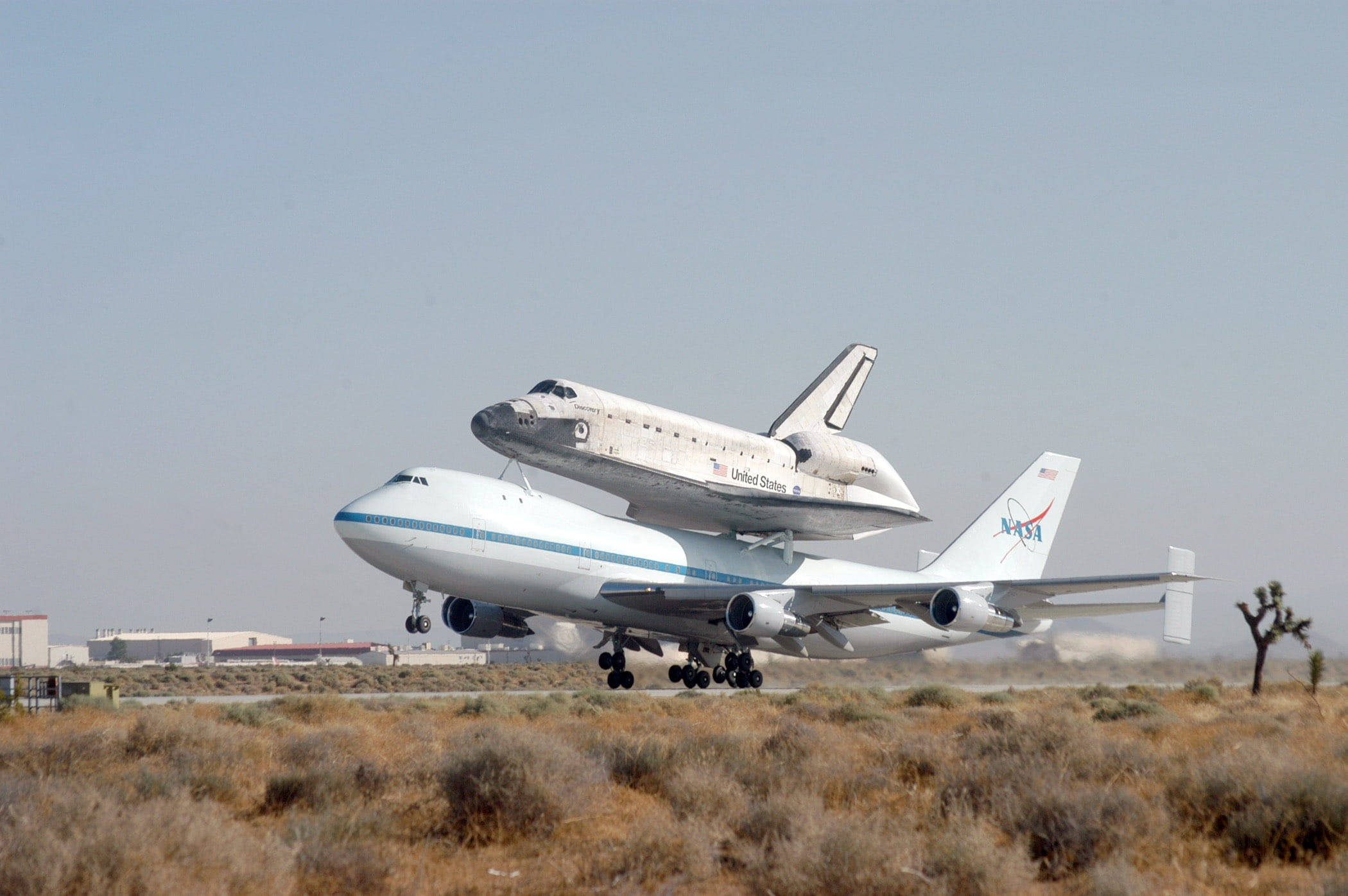 肯尼迪航天中心太空梭運輸機 壁紙 — 一架NASA太空穿梭機安裝在改裝的波音747上，在朦朧的天空下從沙漠跑道起飛。