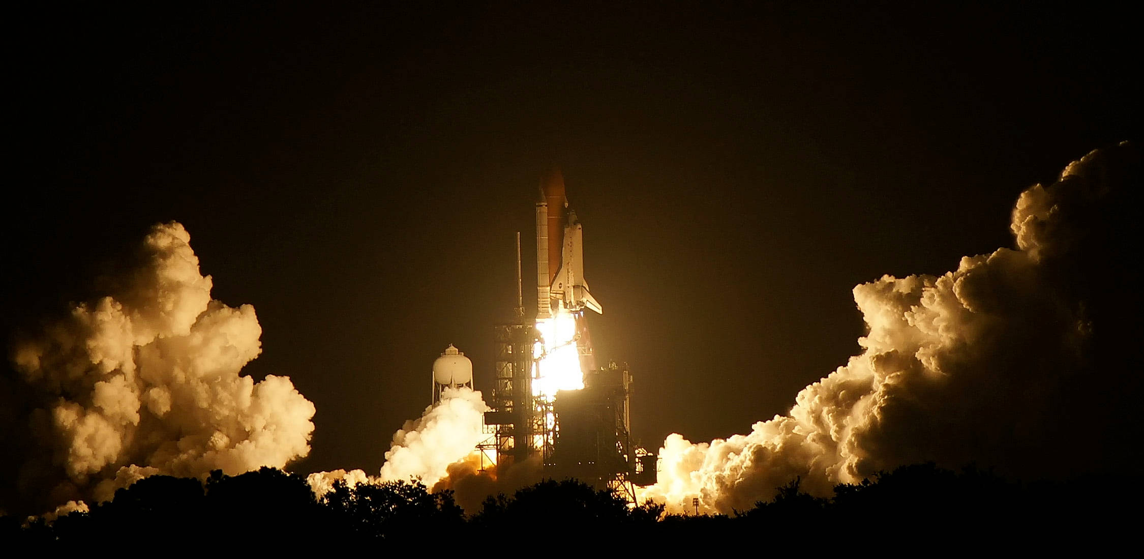肯尼迪航天中心火箭 壁紙 — 一架太空穿梭機在夜間點燃引擎，帶著熾熱的廢氣和翻騰的雲層衝入黑暗。