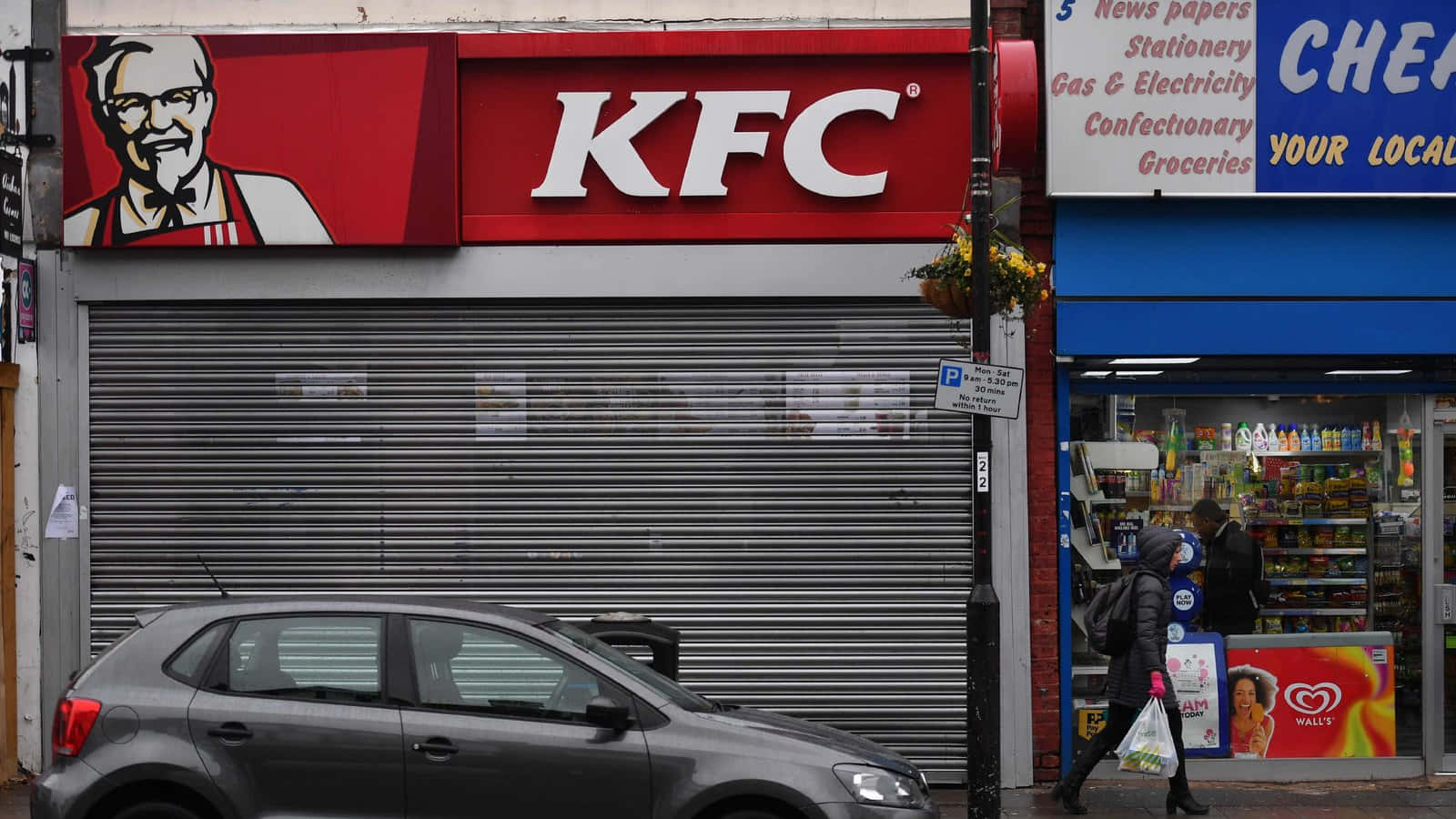 城市街道上關閉的KFC商店，帶金屬捲簾，附近有汽車和行人。