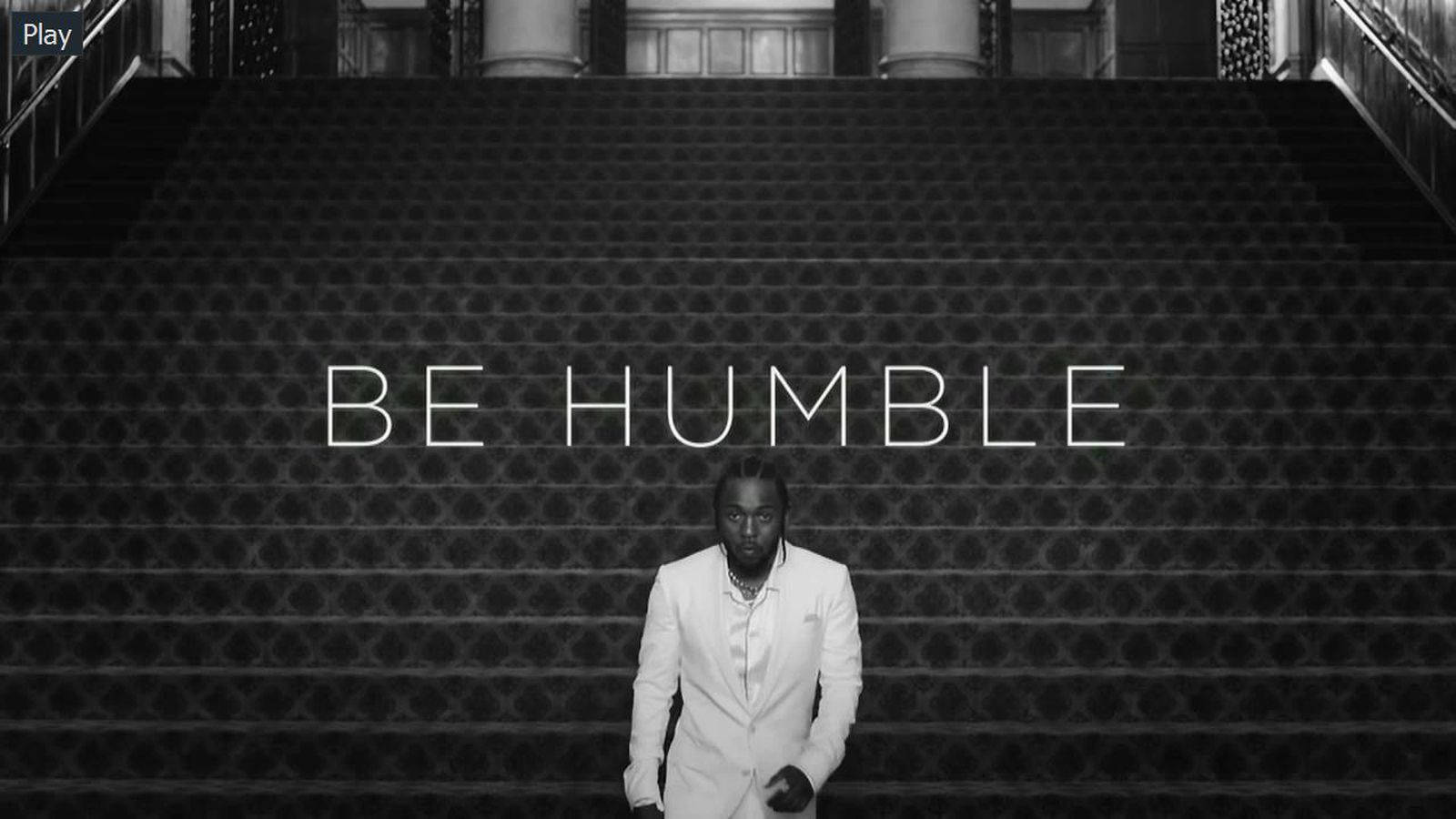 身穿白色西裝的男子站在華麗樓梯底部，帶有「BE HUMBLE」文字。