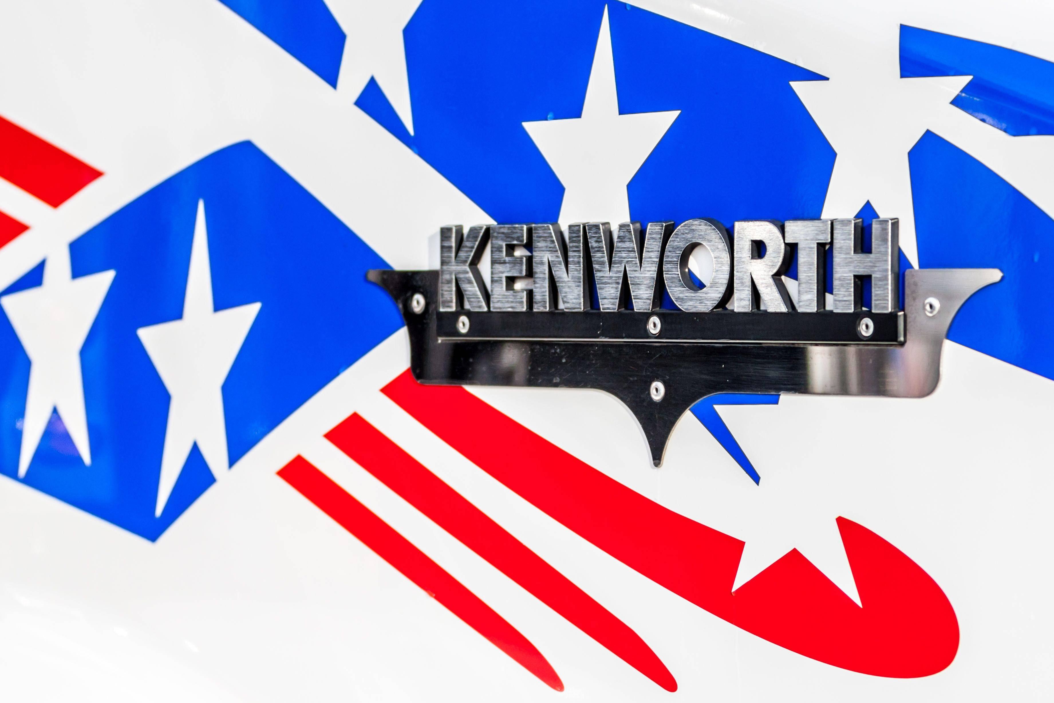 肯沃斯拉絲金屬標誌 壁紙 — 卡車上安裝的鍍鉻 Kenworth 標誌特寫，帶有醒目的紅、白、藍星條紋圖案。
