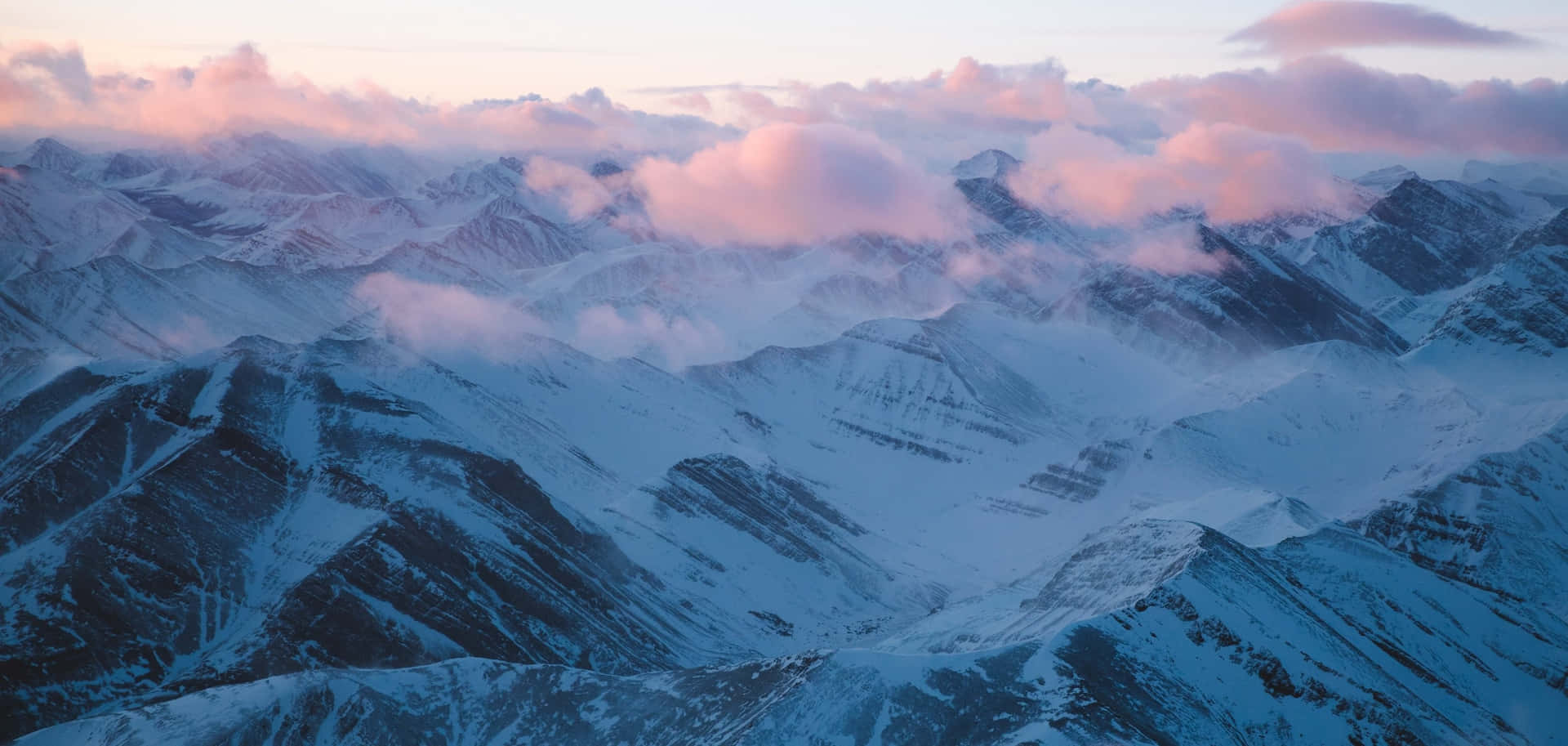 粉紅色和藍色黎明雲層下的雪山山脈