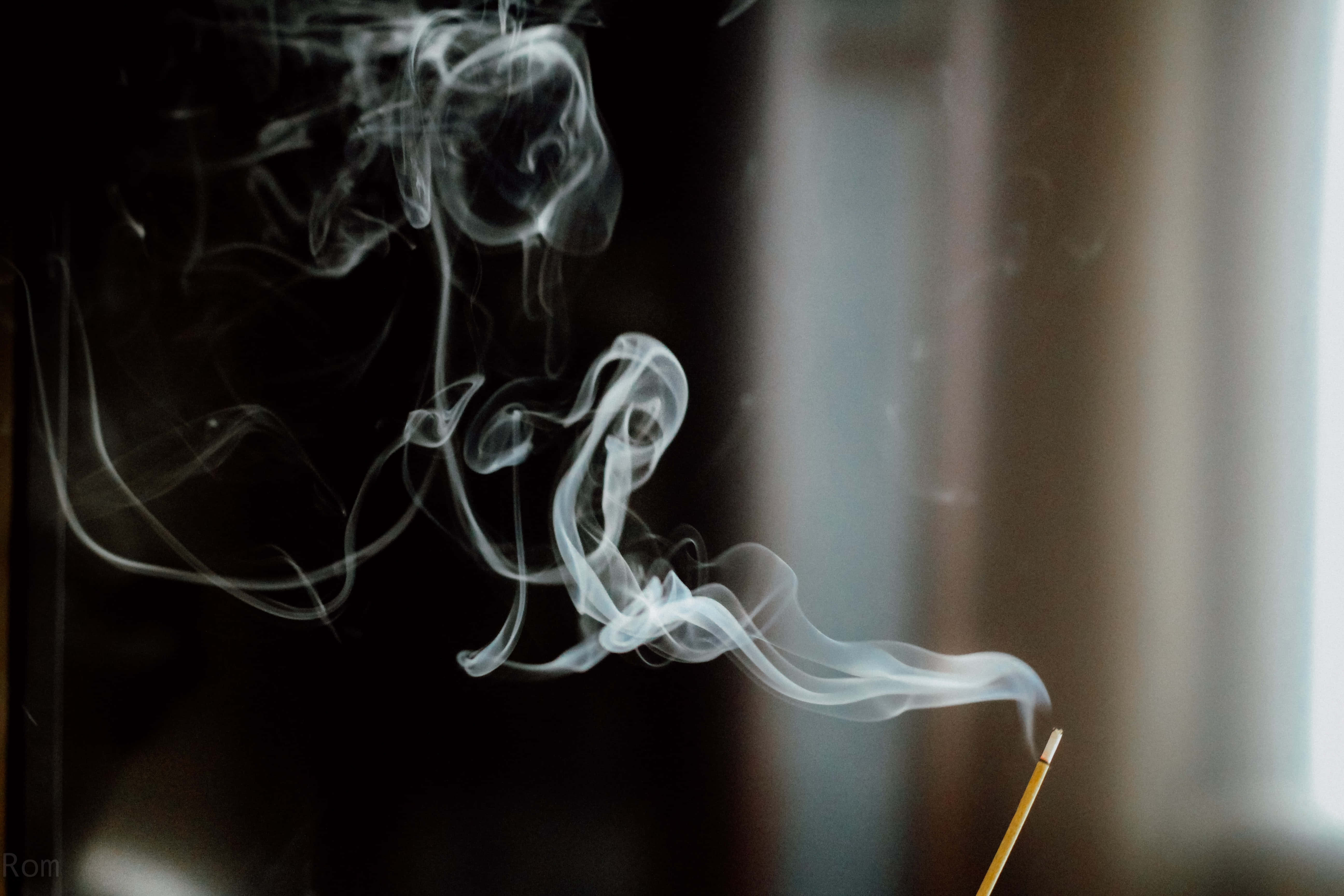 背景為煙霧山脈的抽象自然風景 壁紙 — 細緻的白煙香薰在柔和光線下，於黑暗模糊的背景中優雅地盤旋。