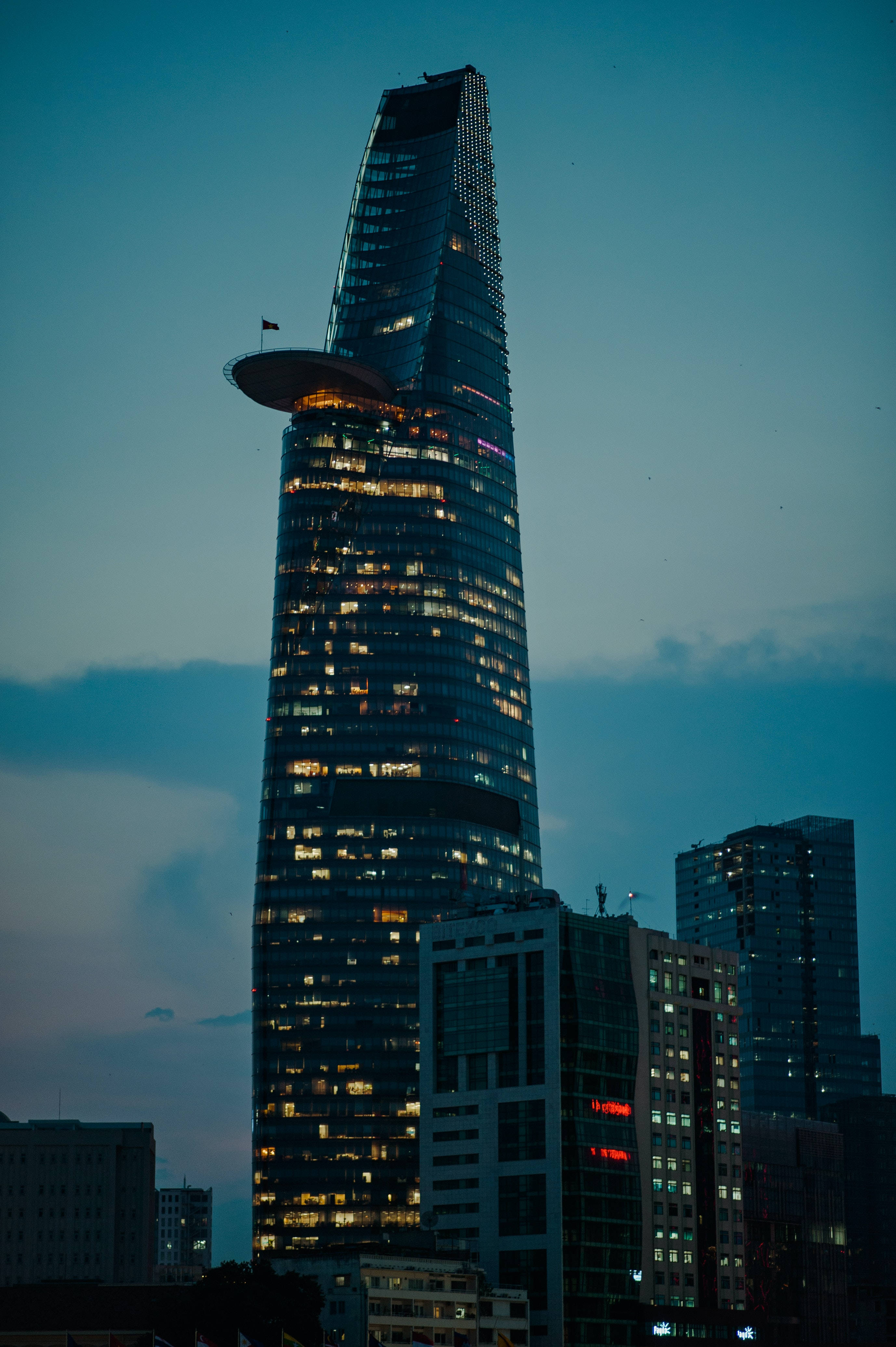 胡志明市Bitexco金融塔 壁紙 — 一座高聳的摩天大樓，帶有發光的窗戶和獨特的圓形頂部，矗立在深藍色的天空下，構成城市景觀。