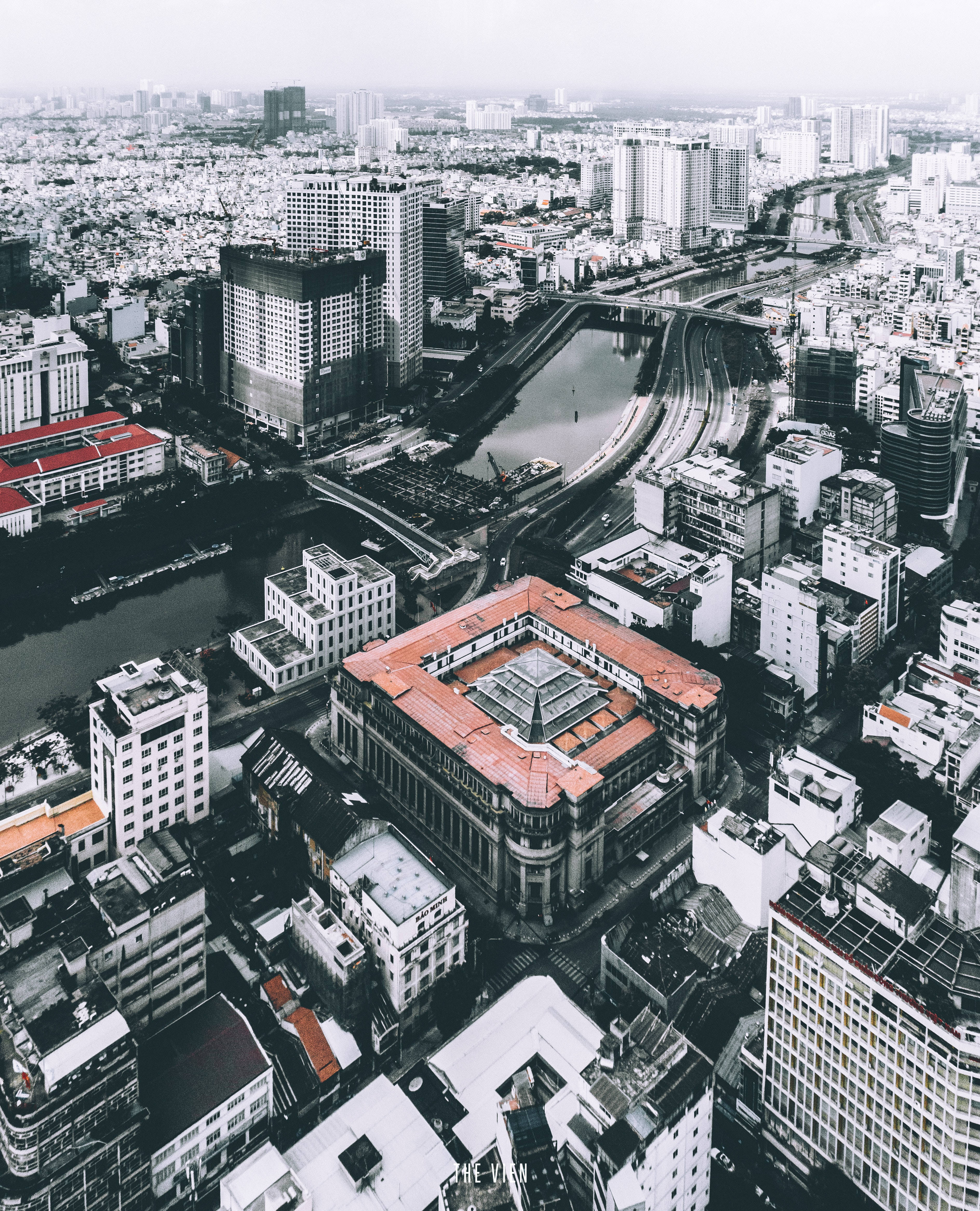 胡志明市國家銀行 壁紙 — 陰天天空下，一條蜿蜒的河流穿過現代和傳統建築的密集城市景觀的鳥瞰圖。