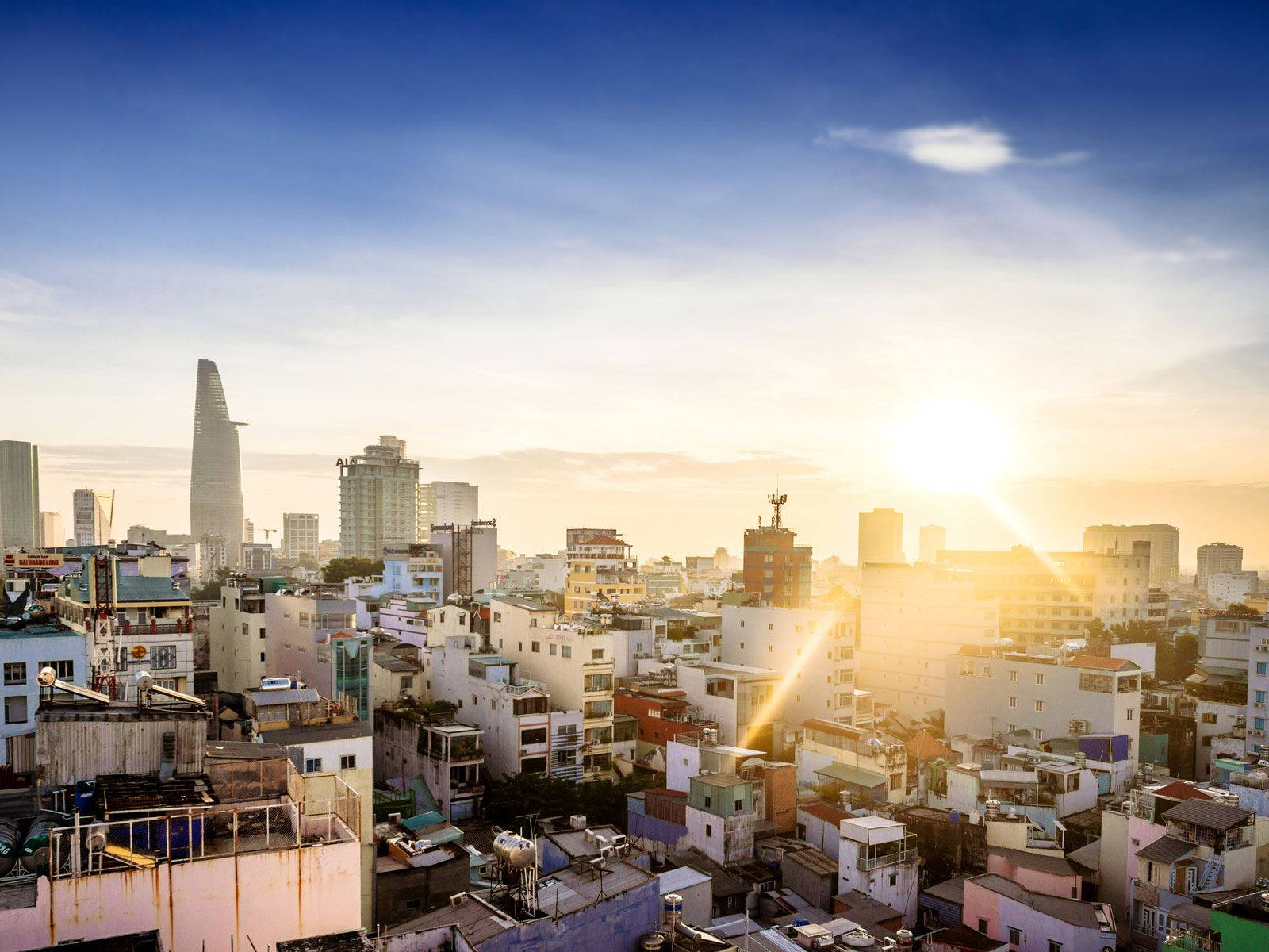 胡志明市晨曦 壁紙 — 日出將密集的城市天際線沐浴在金色光芒中，現代塔樓聳立在密密麻麻的住宅建築之上。