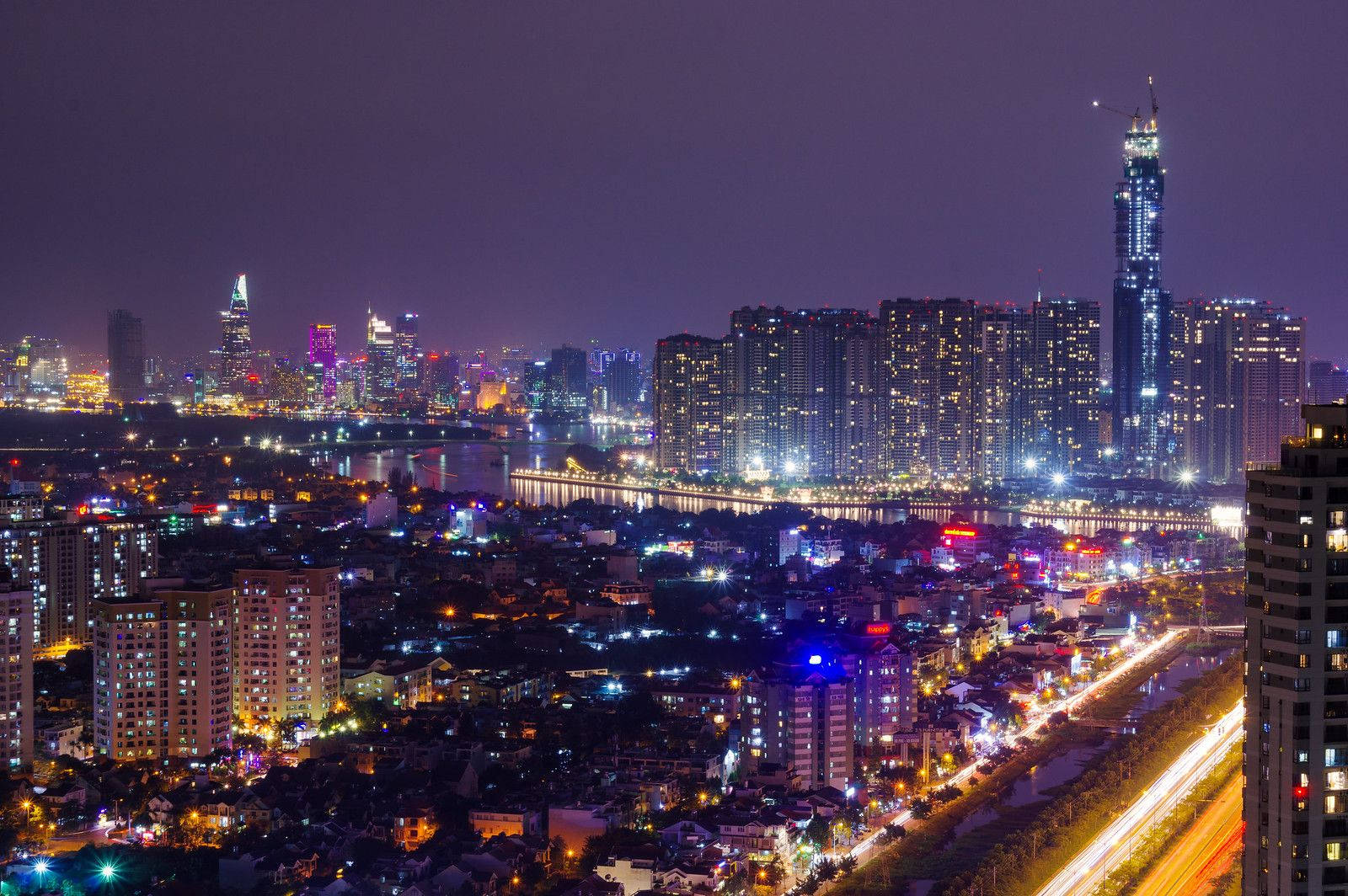 胡志明市紫夜天際 壁紙 — 充滿活力的夜間城市景觀，河邊有發光的摩天大樓和交通燈跡。