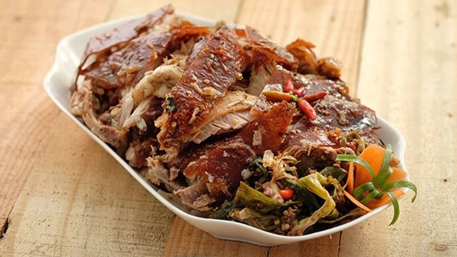 Lechon Paksiw 壁紙 — 脆皮烤豬肉配香草和紅蘿蔔，盛載於白色碟中，置於鄉村風木桌上。