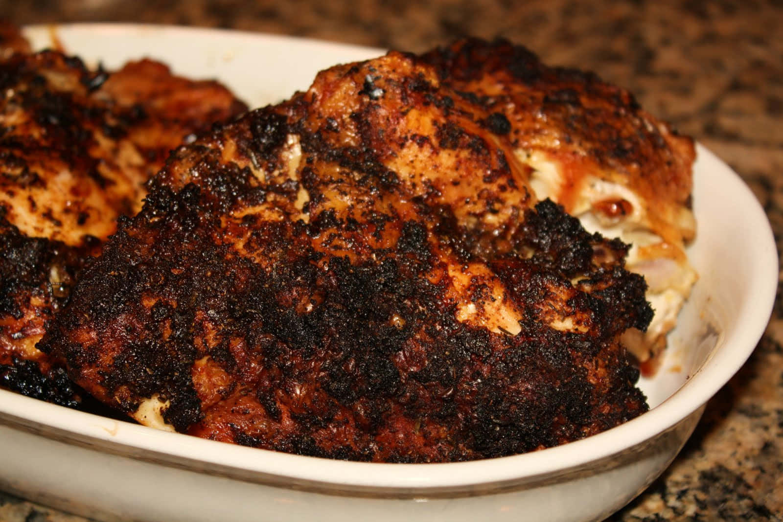Blackened Chicken 桌布 壁紙 — 脆皮焦黑的雞塊在白色陶瓷盤中閃閃發光，置於斑點檯面上。