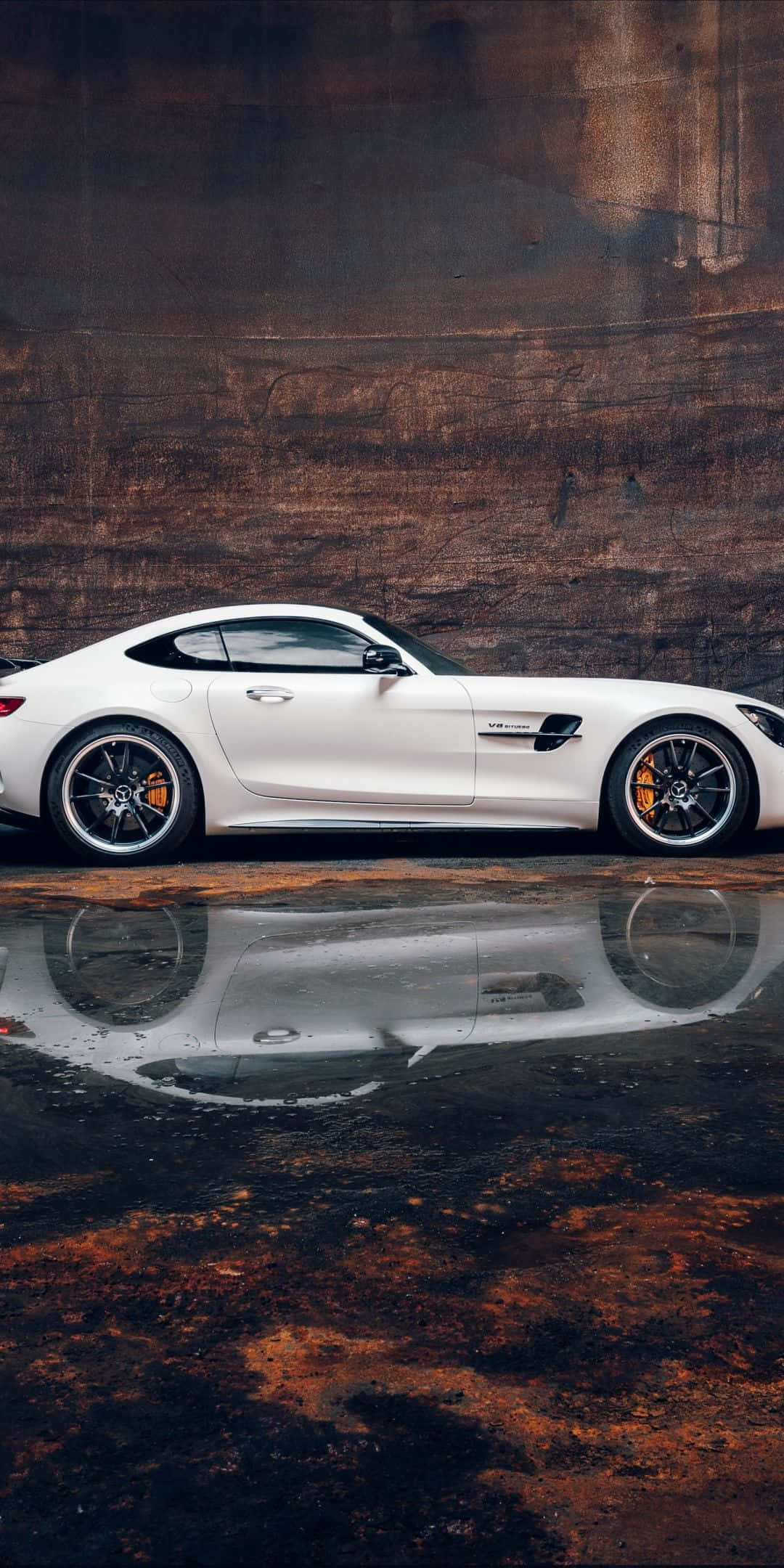 脈動的力量——梅賽德斯AMG GT R 壁紙 — 一輛時尚的白色跑車在陰暗燈光下，映照在一個水坑中，背景是風化的棕色牆壁。
