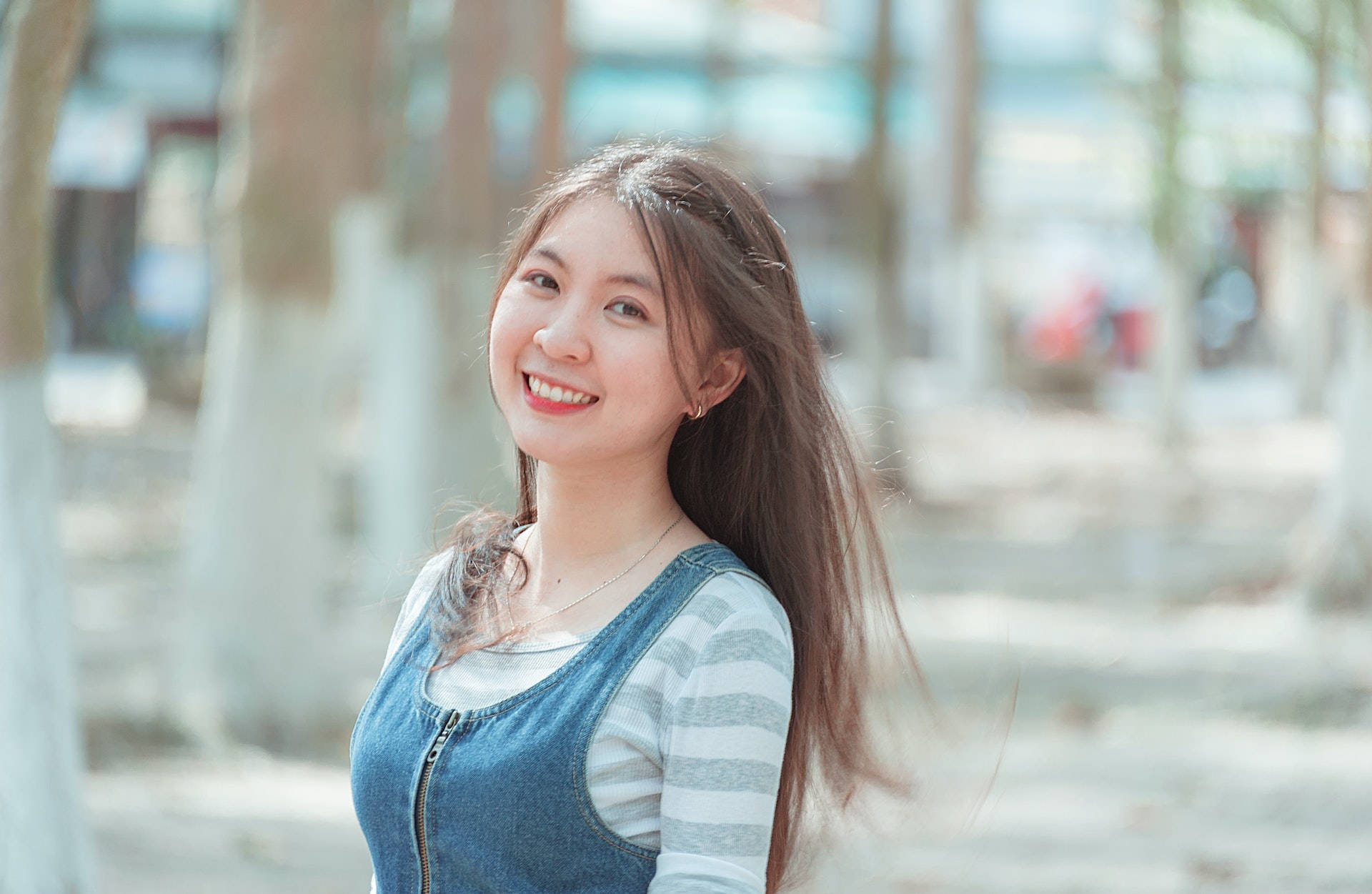 年輕女性在陽光明媚的日子裡穿著牛仔連身褲在戶外微笑。