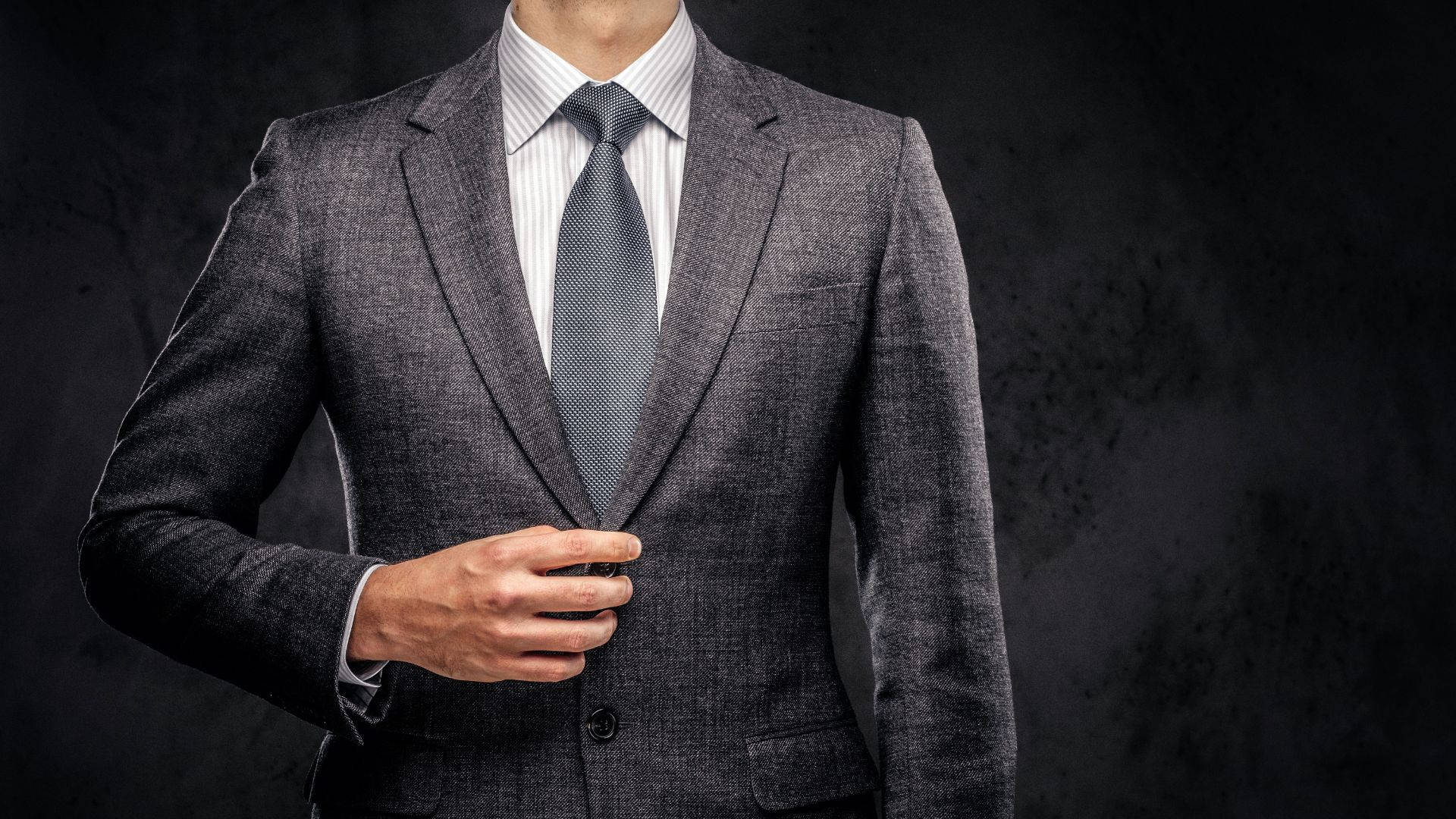自信商務人士灰色西裝 壁紙 — 一位身穿俐落灰色西裝的男子在深色紋理背景前調整領帶。