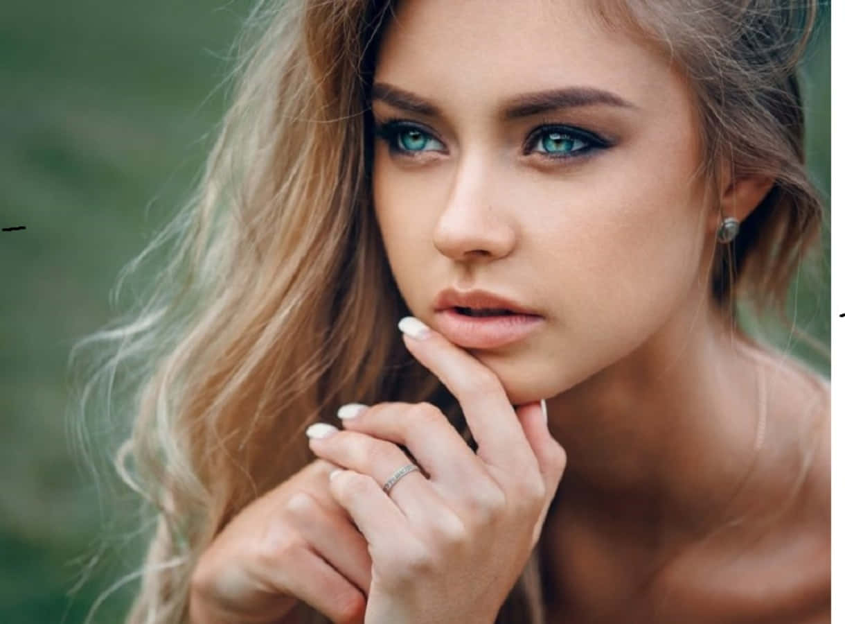 一位擁有藍眼睛和金色頭髮的女性在戶外輕輕觸摸下巴。