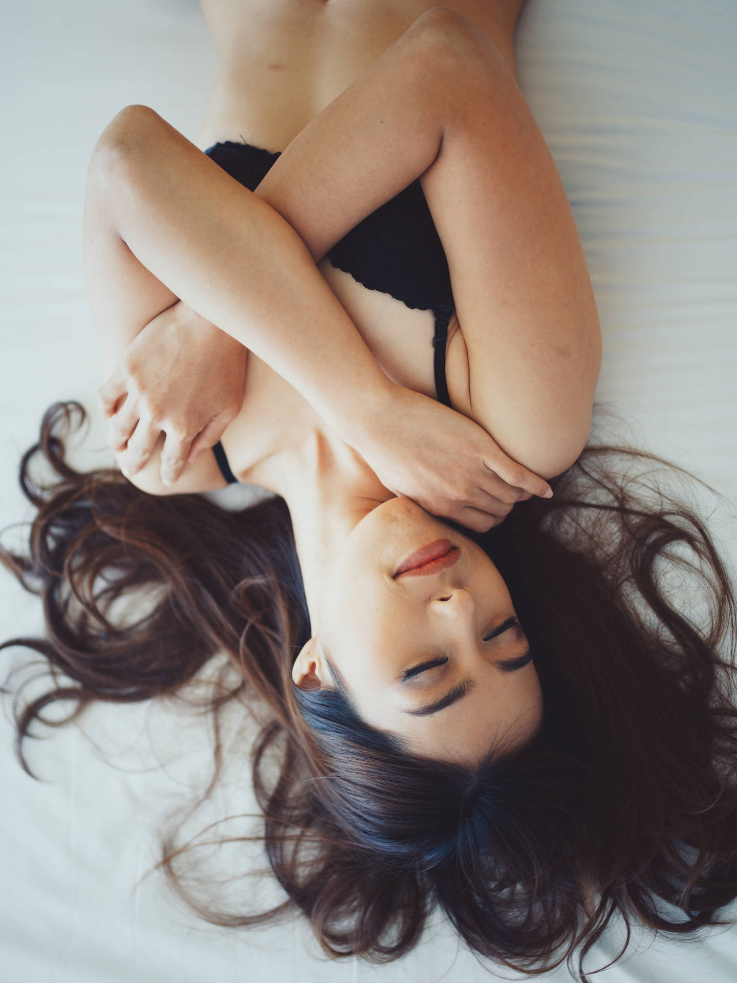 一位穿著黑色內衣的女性在白色床上閉著眼睛安詳地休息。