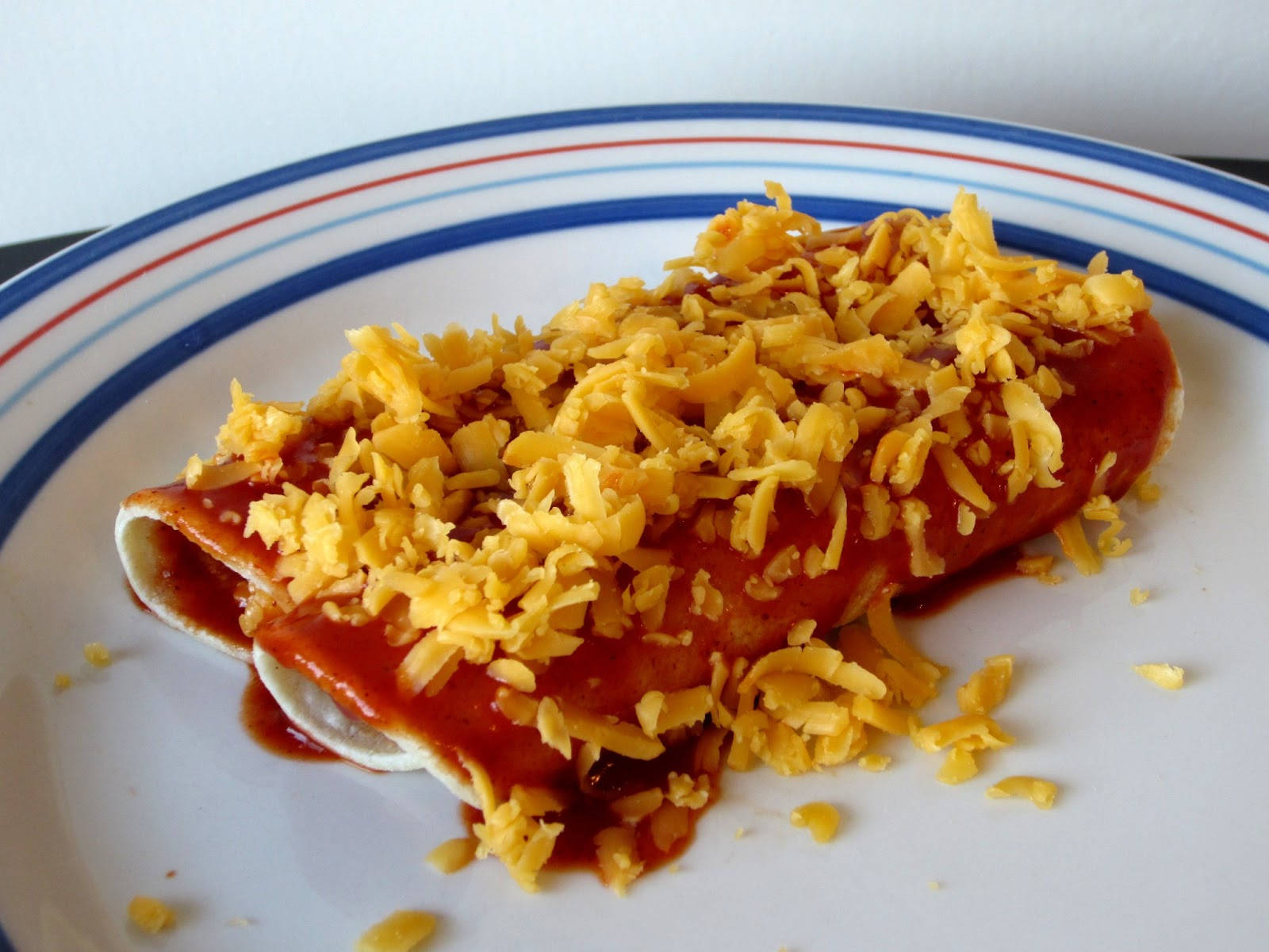 自家製奶酪 enchiladas 壁紙 — 兩條捲好的墨西哥捲餅浸在紅醬中，上面撒上切達起司絲，放在條紋盤子上。