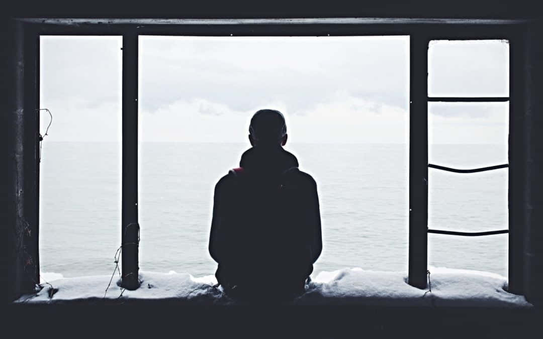 在陰沉的冬日，一個人坐在積雪的窗台上眺望大海