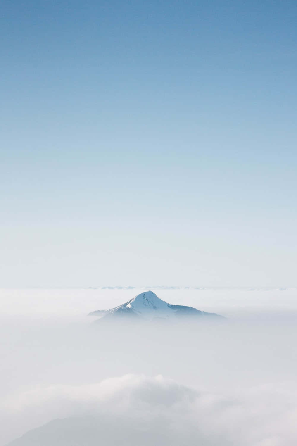 在清澈藍天下，從雲海中浮現的雪山頂峰。