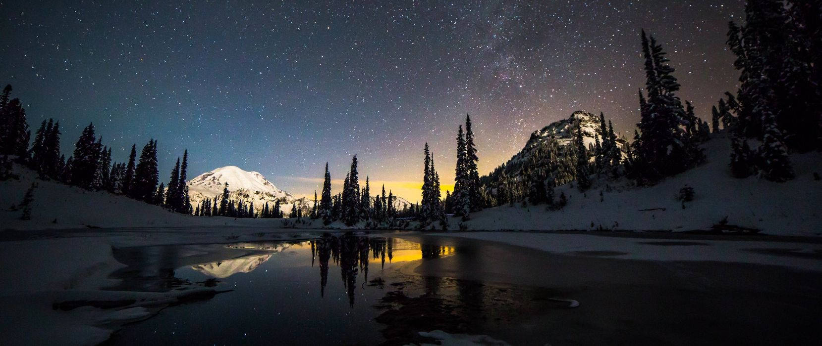 白雪覆蓋的山間湖泊，在繁星點點的夜空下，松樹和發光的地平線倒影。