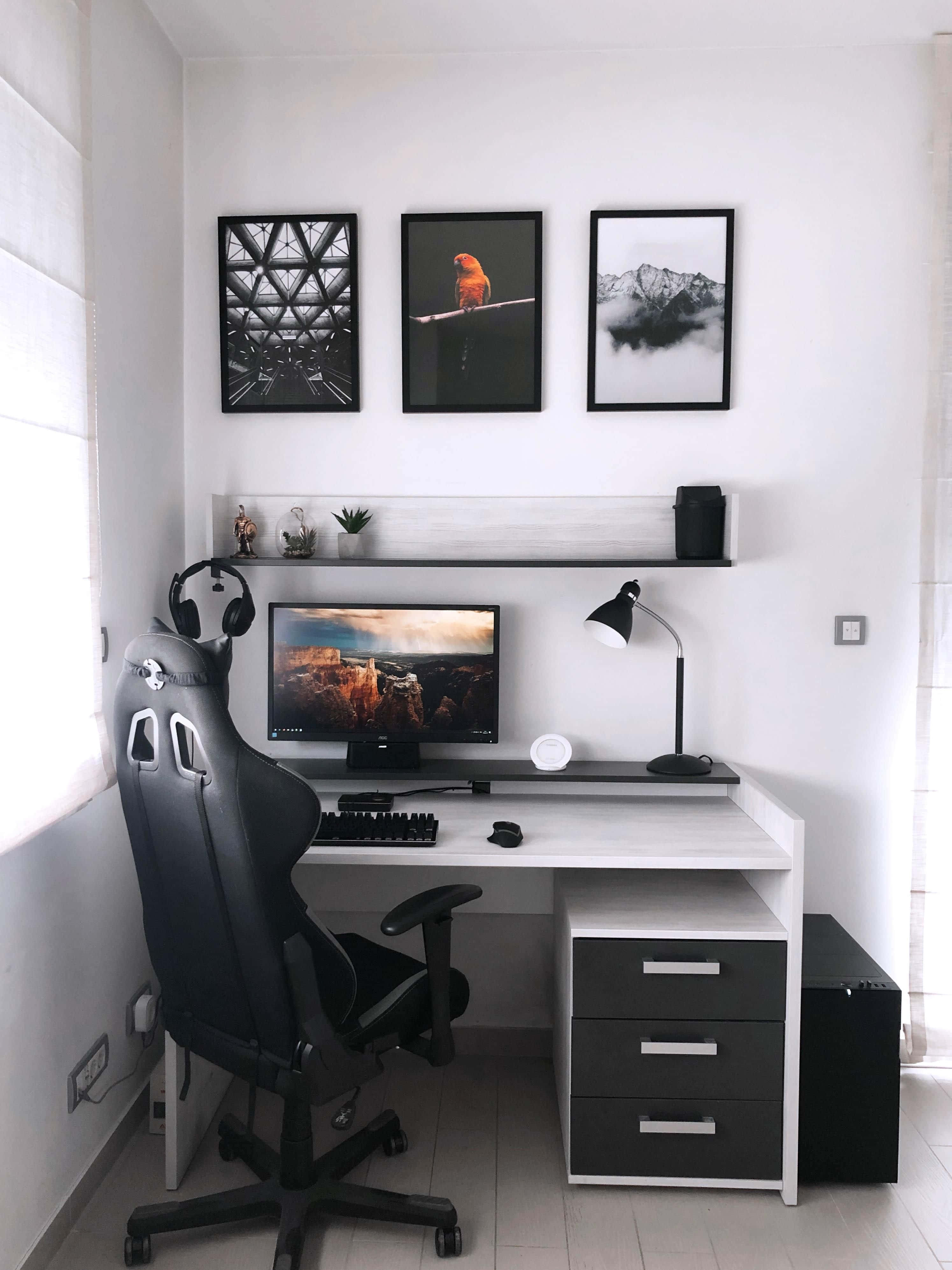 Gaming Accessories 桌布 壁紙 — 自然光下的簡約家居辦公室，配有白色書桌、黑色電競椅和裱框牆面藝術品。