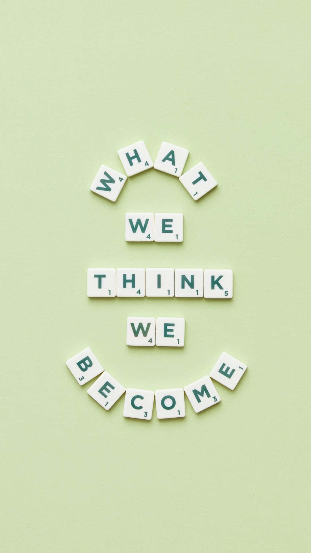 Scrabble 字母牌排列在綠色背景上拼出「What we think we become」。