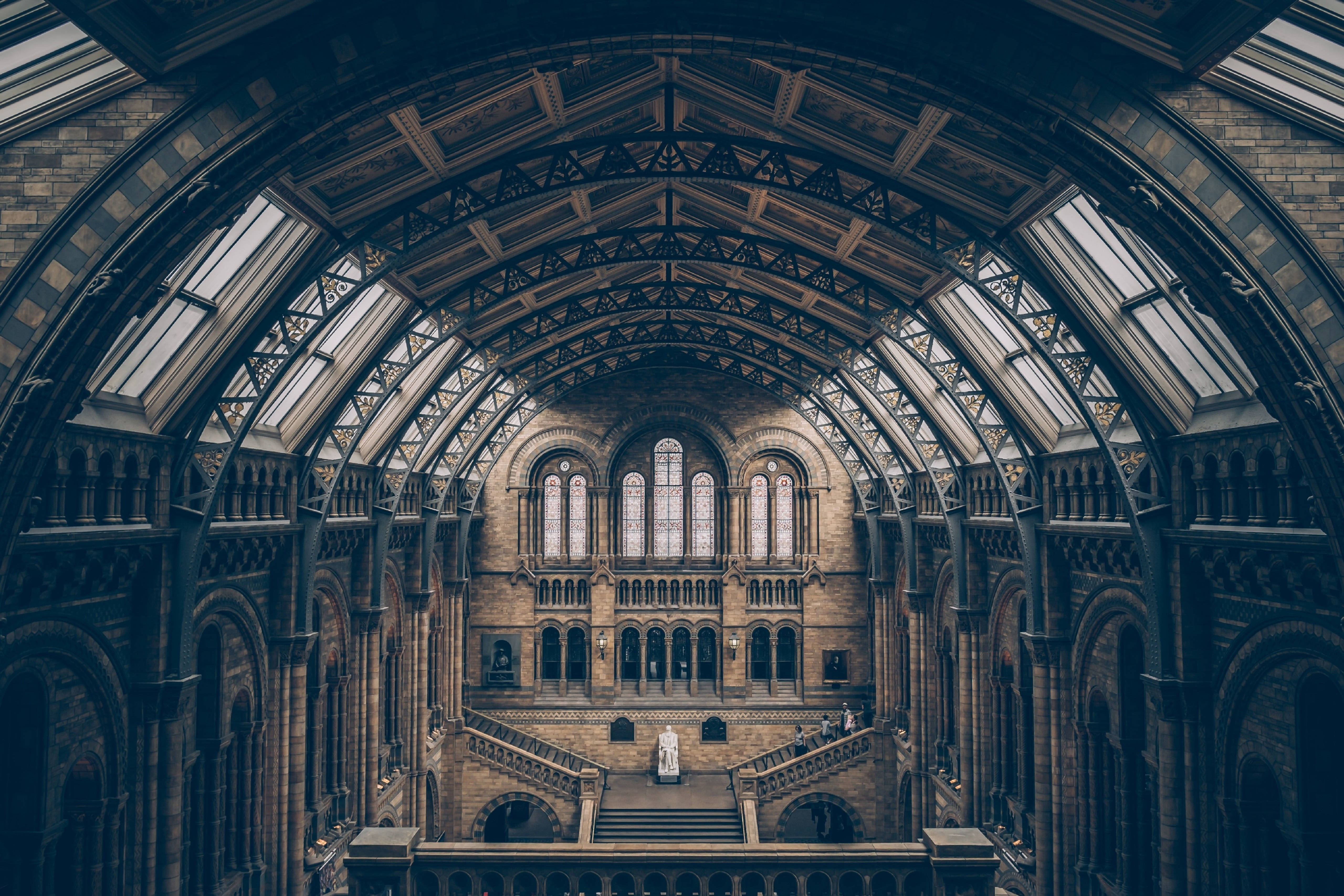 自然歷史博物館建築壯觀景觀 壁紙 — 歷史博物館的宏偉拱形內部，帶有精緻的鐵藝玻璃天花板和石樓梯。